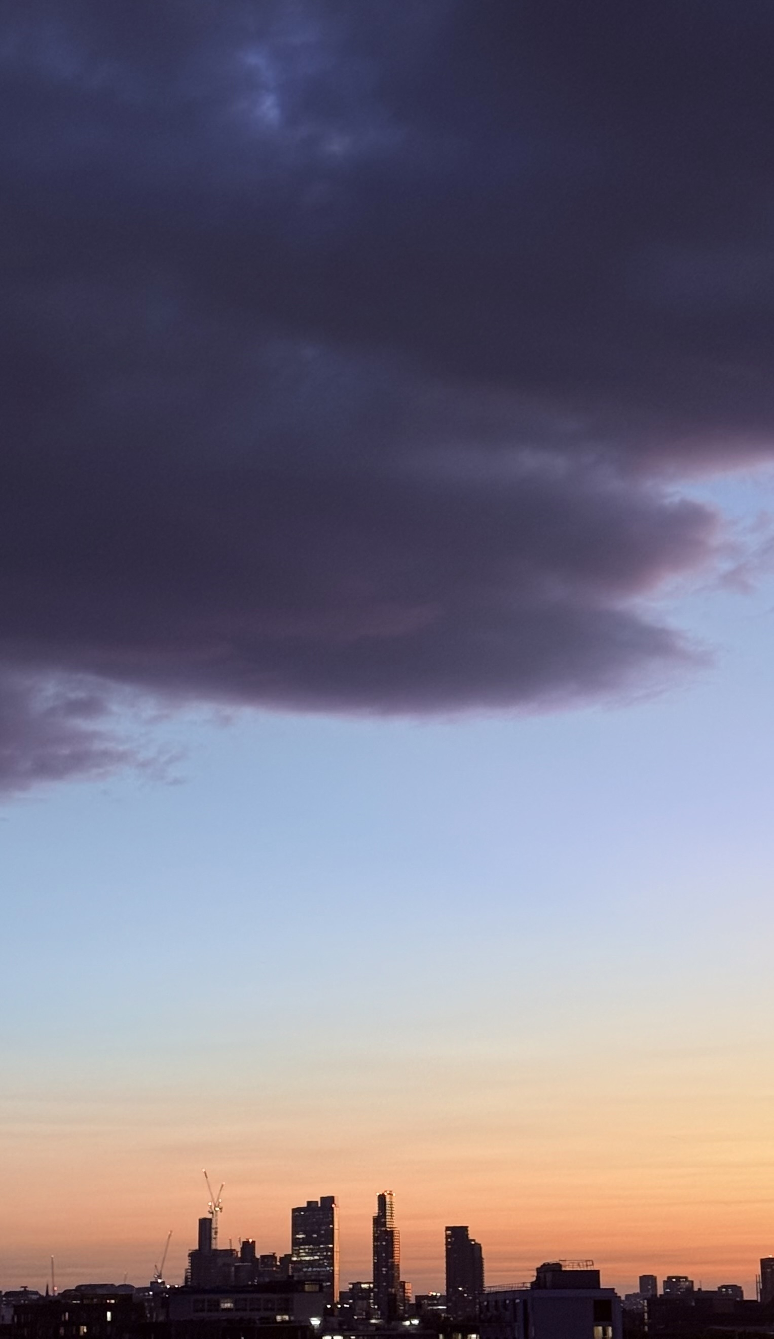 A dark cloud high above distant towers at sunset.