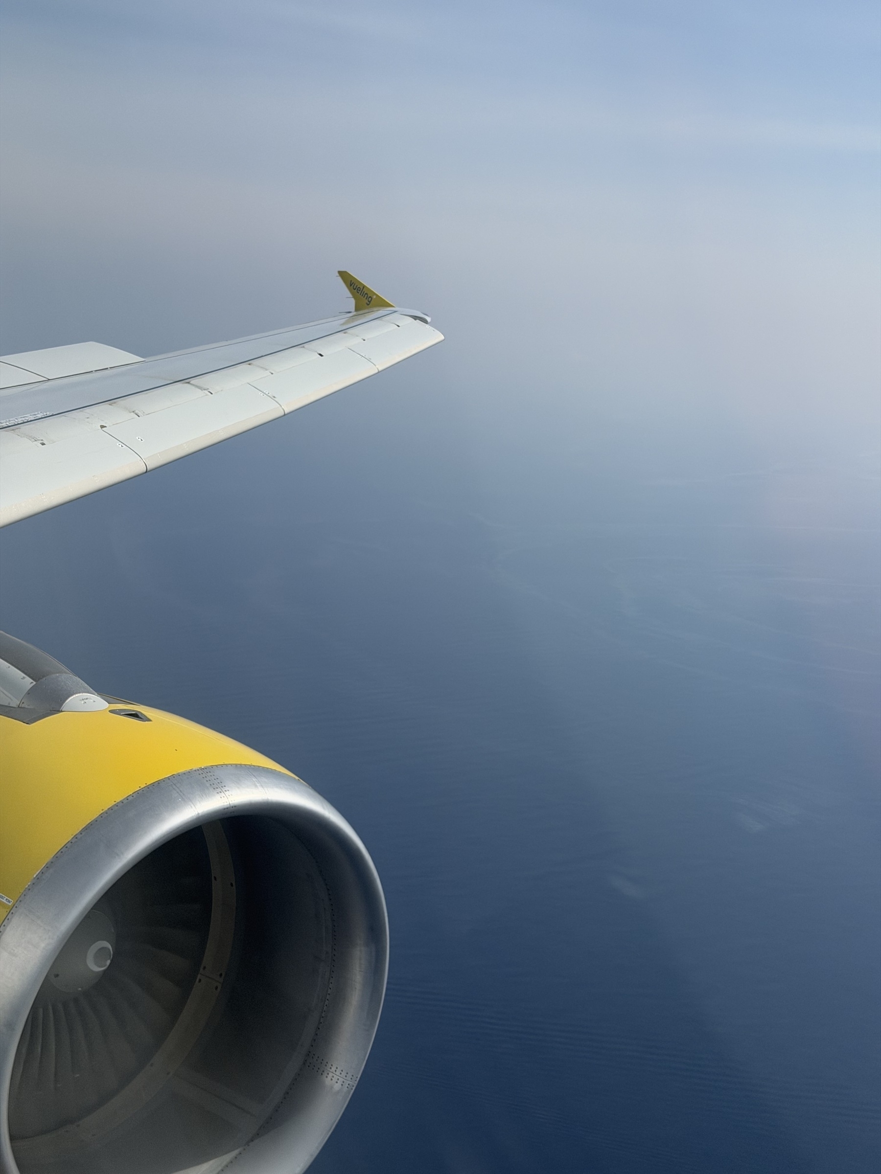 Looking out of a plane window at the engine and wing, flying high over the sea.