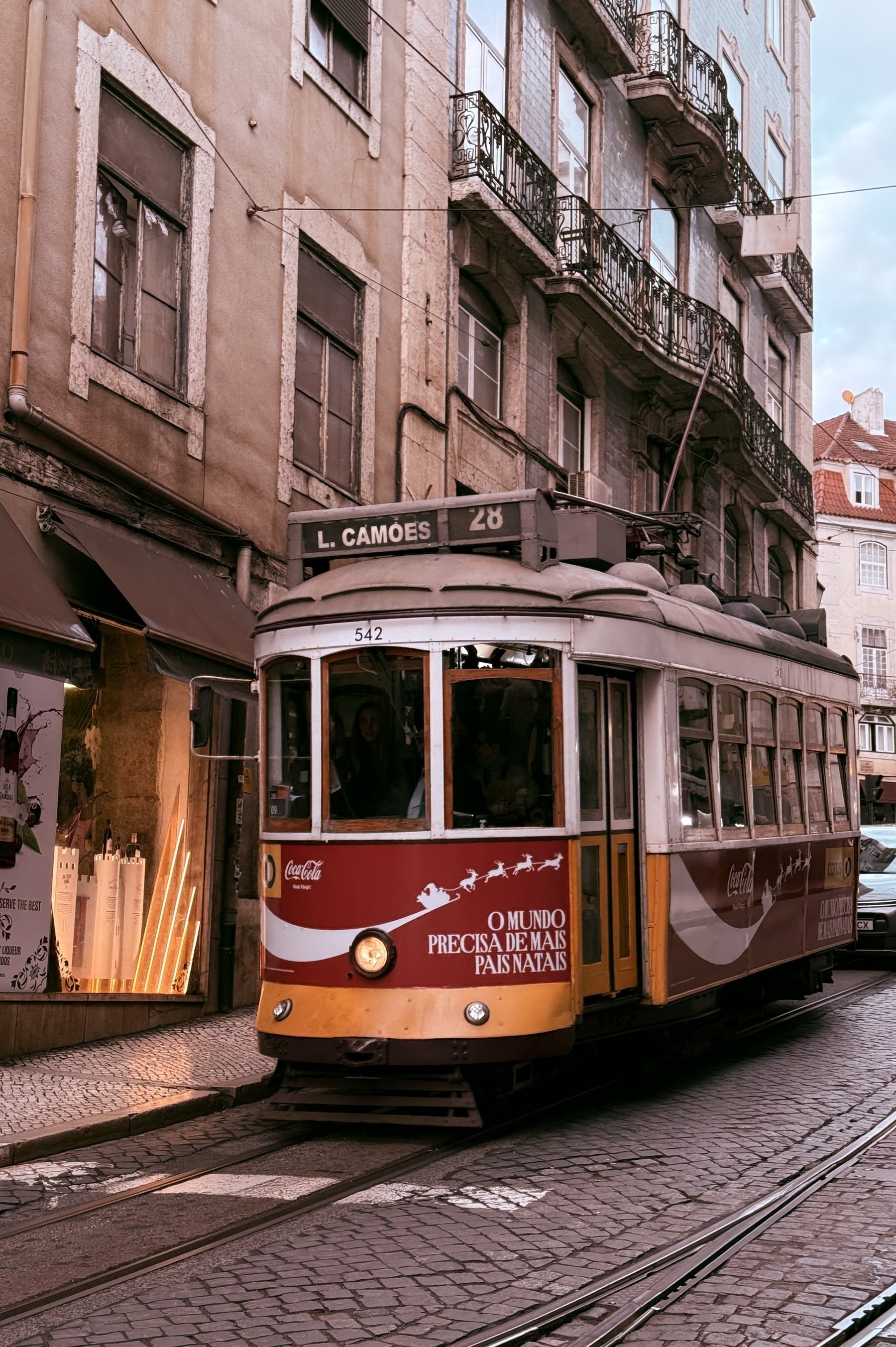 A small one carriage tram travelling down a cobbled street in Lisbon.