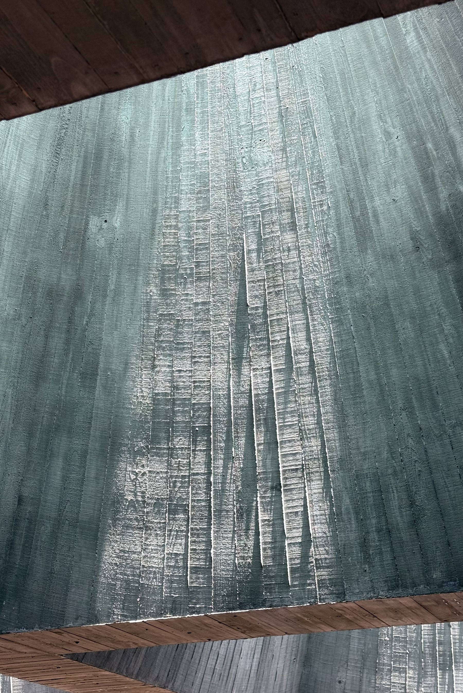 The side of a concrete skylight lit from above by sunlight, highlighting the texture of the concrete.