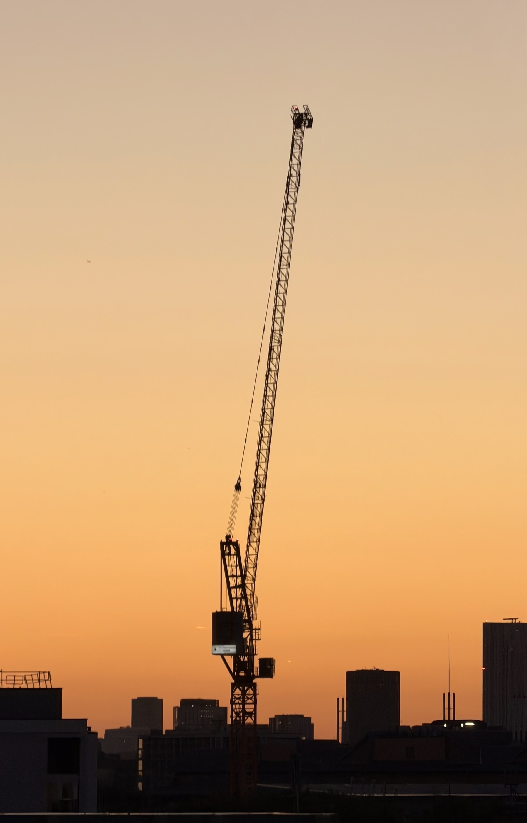 A crane reaching up in to an orange sky.