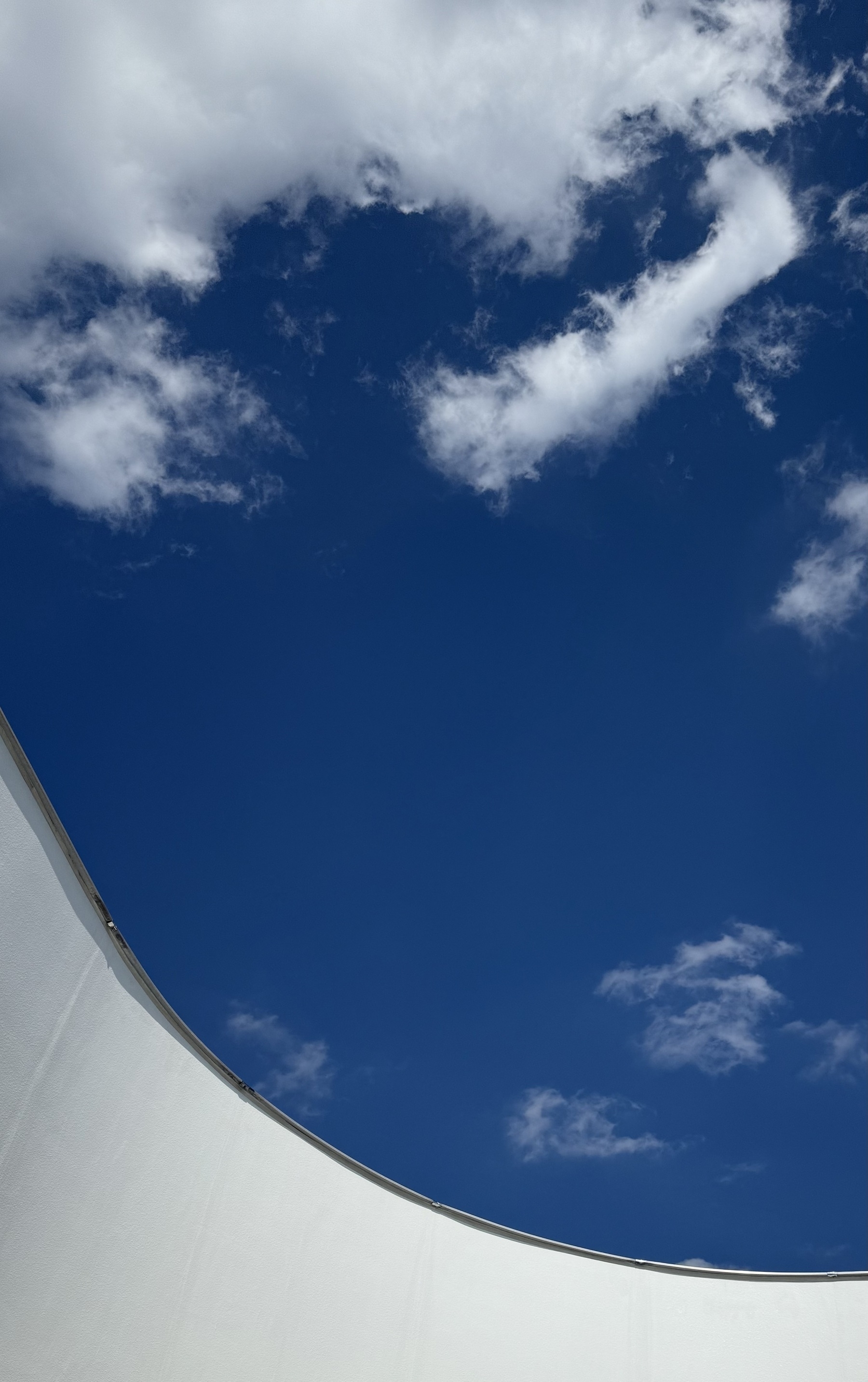 A curved white wall with a deep blue sky above, with crisp white clouds.
