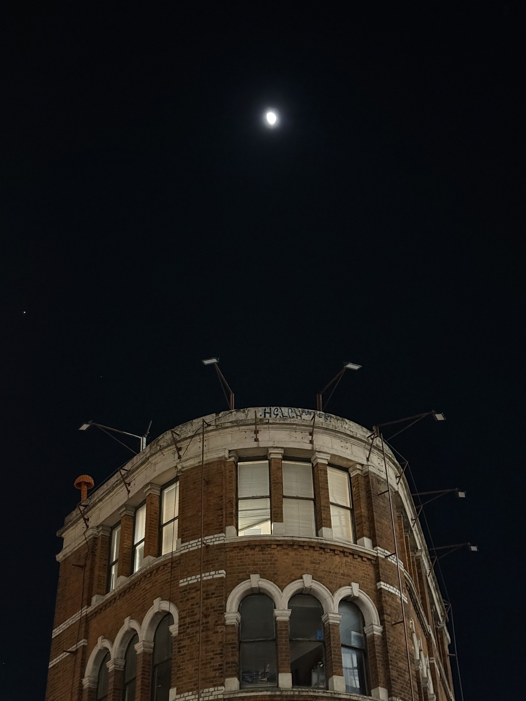 A brick building with a rounded front against an inky black sky, with the moon high above.