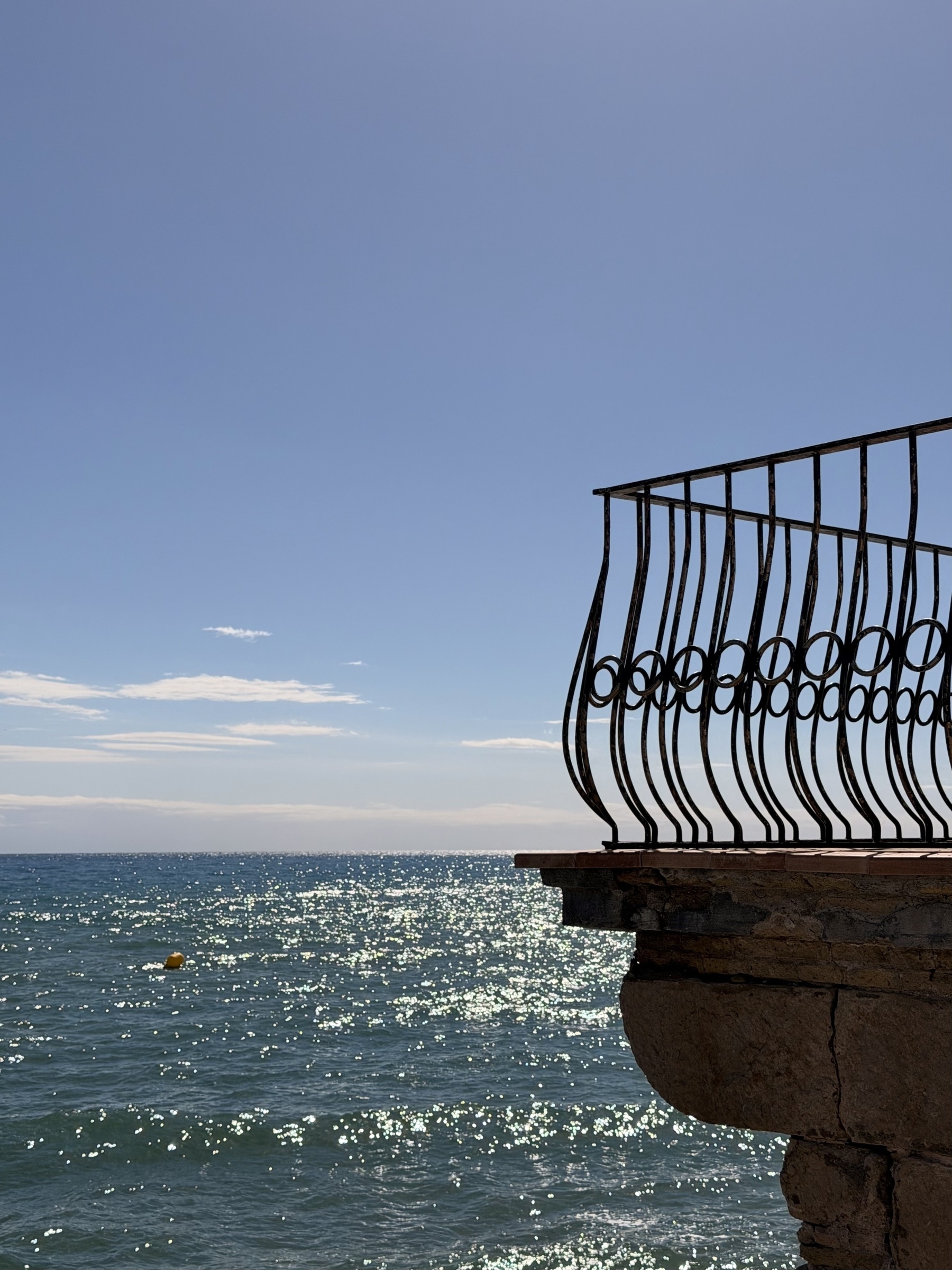 A stone balcony with a metal railing overlooking the sea.
