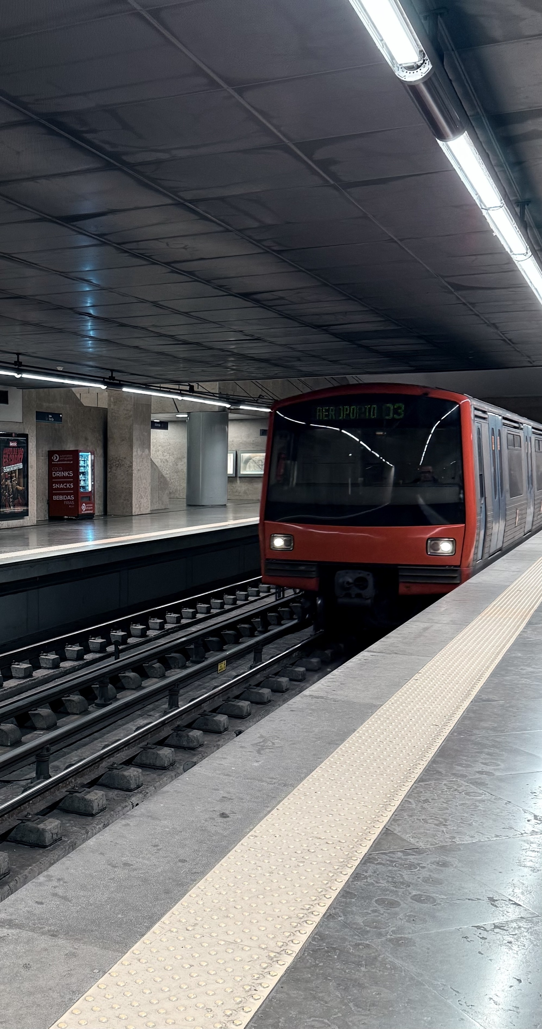 A red fronted metro train heading to Lisbon airport.