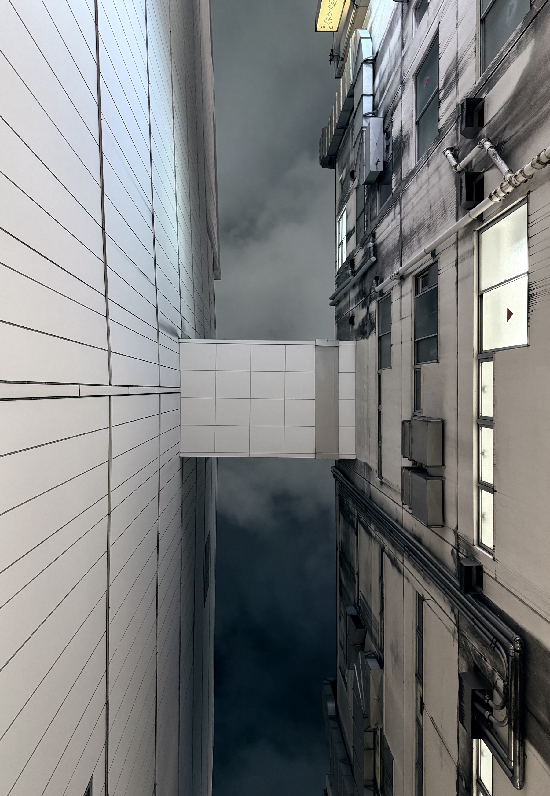 Looking directly up at a skybridge connecting two buildings across a narrow alley.