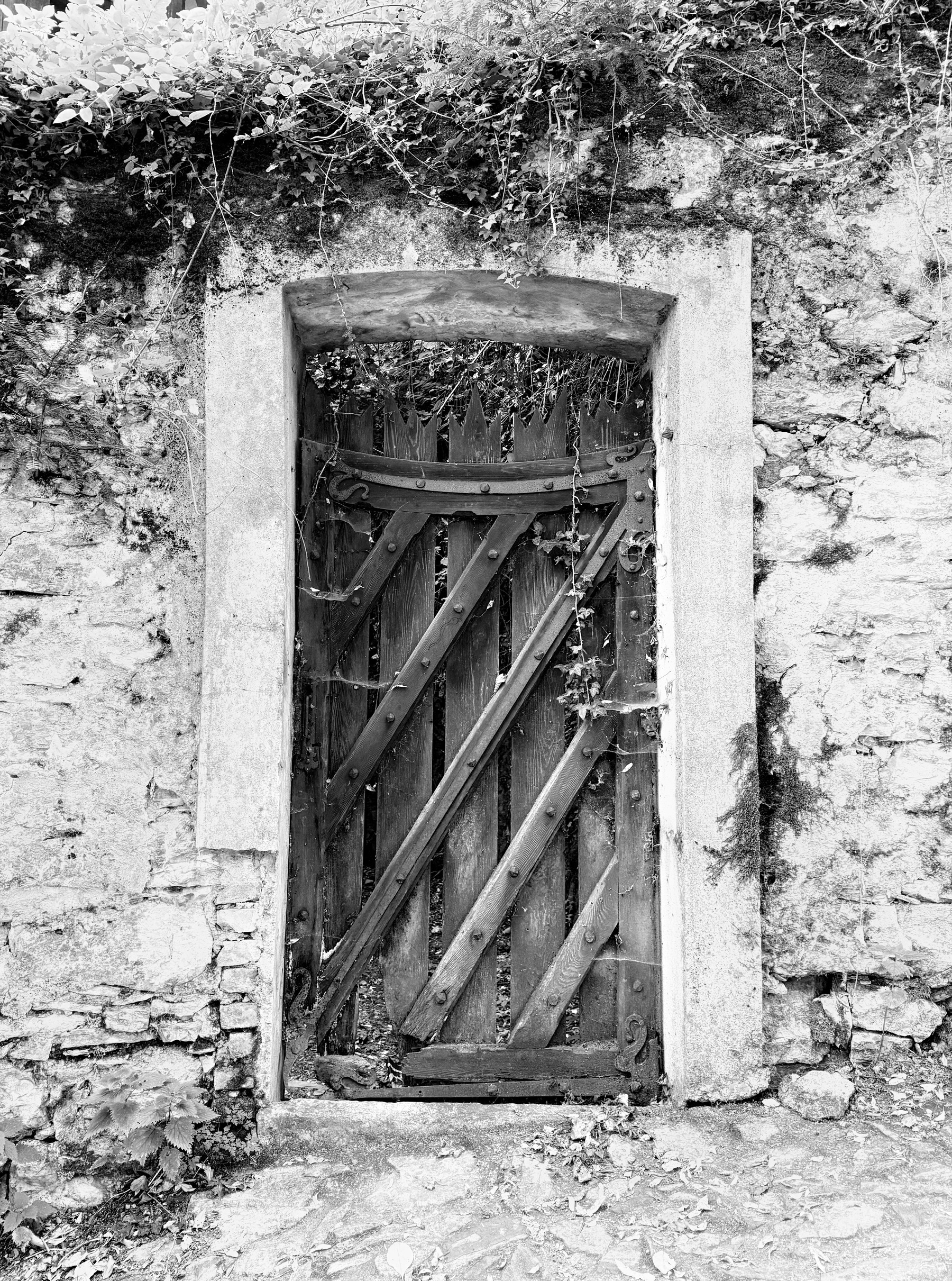 A black and white photo of a wooden gate in a stone wall.