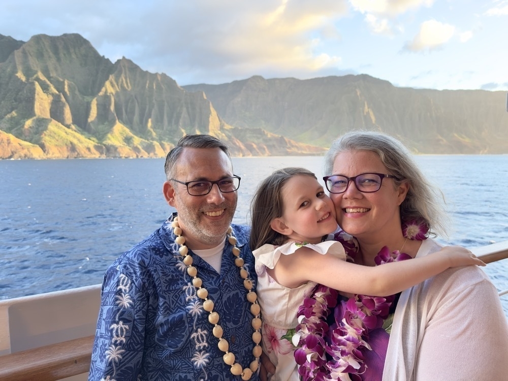 Me, my daughter, and wife standing together on a cruise ship with the ocean and the island of Kaua’i in the background.