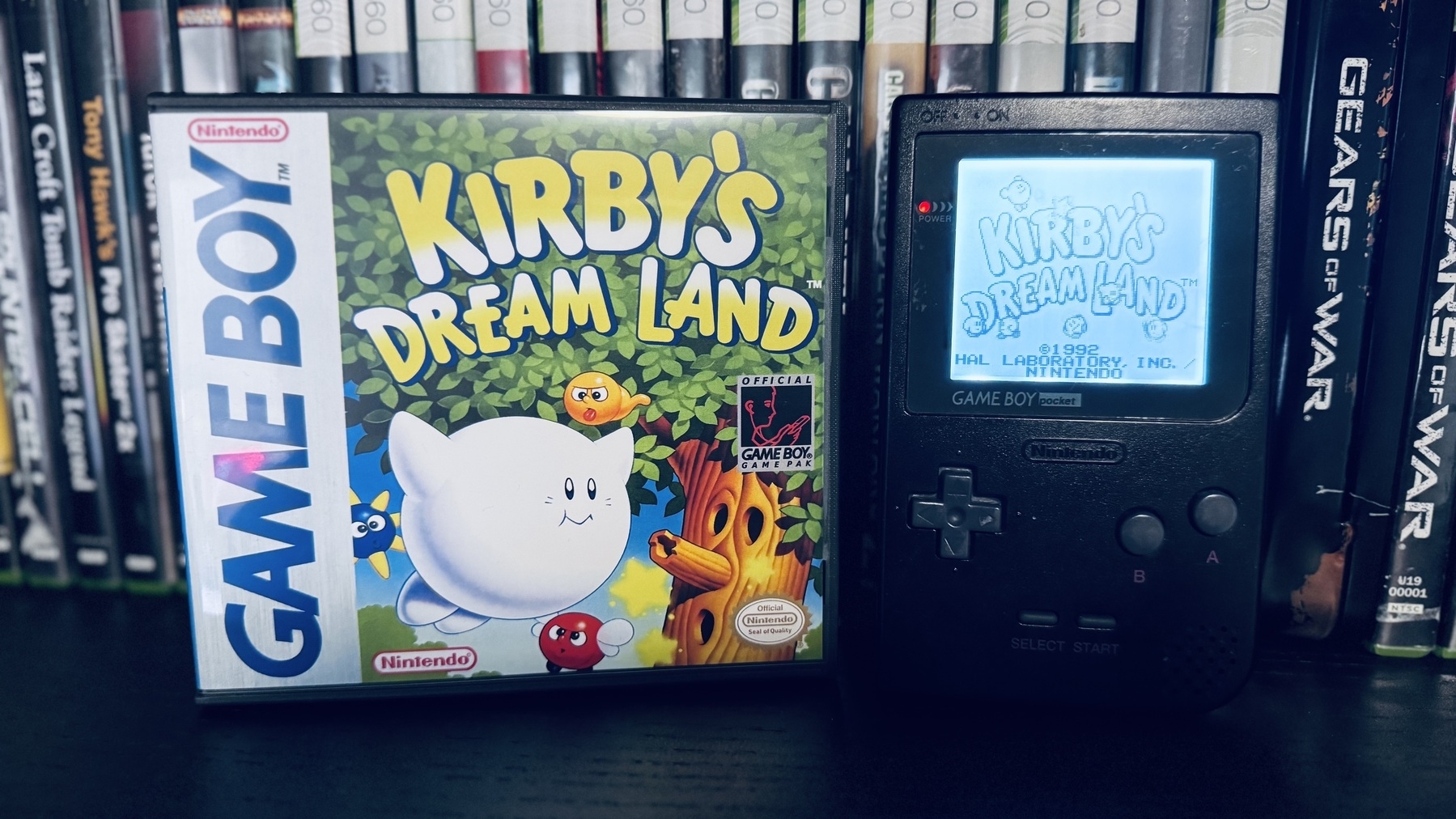Auto-generated description: A Game Boy game box for Kirby’s Dream Land is displayed next to a Game Boy with the game’s title screen.