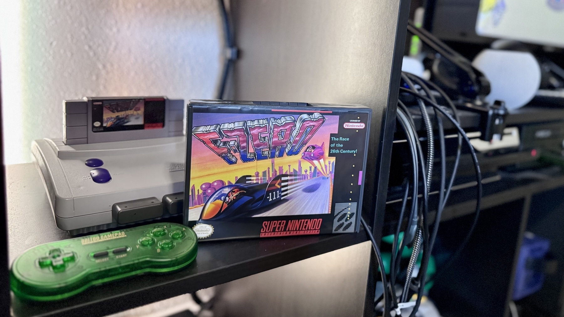 Auto-generated description: A retro gaming setup features a Super Nintendo console, cartridge, game controller, and an F-Zero game box.
