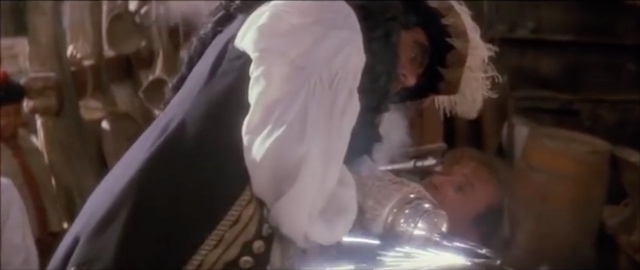 A screenshot from the film Hook, where Dustin Hoffman has Robin Williams pinned down, while Hoffman is sharpening his hook on a grinder.