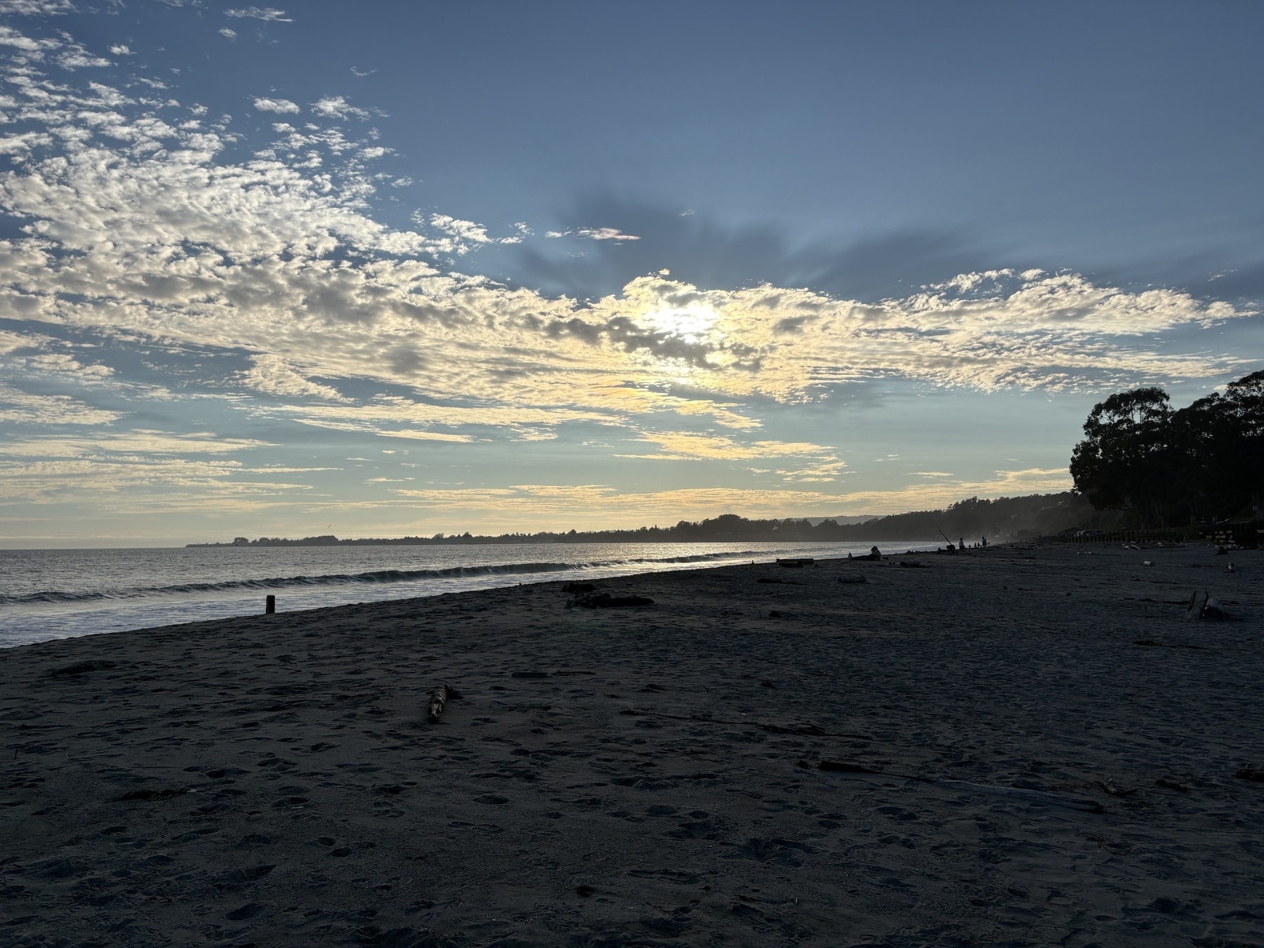 A serene beach scene at sunset with scattered clouds and calm waves.
