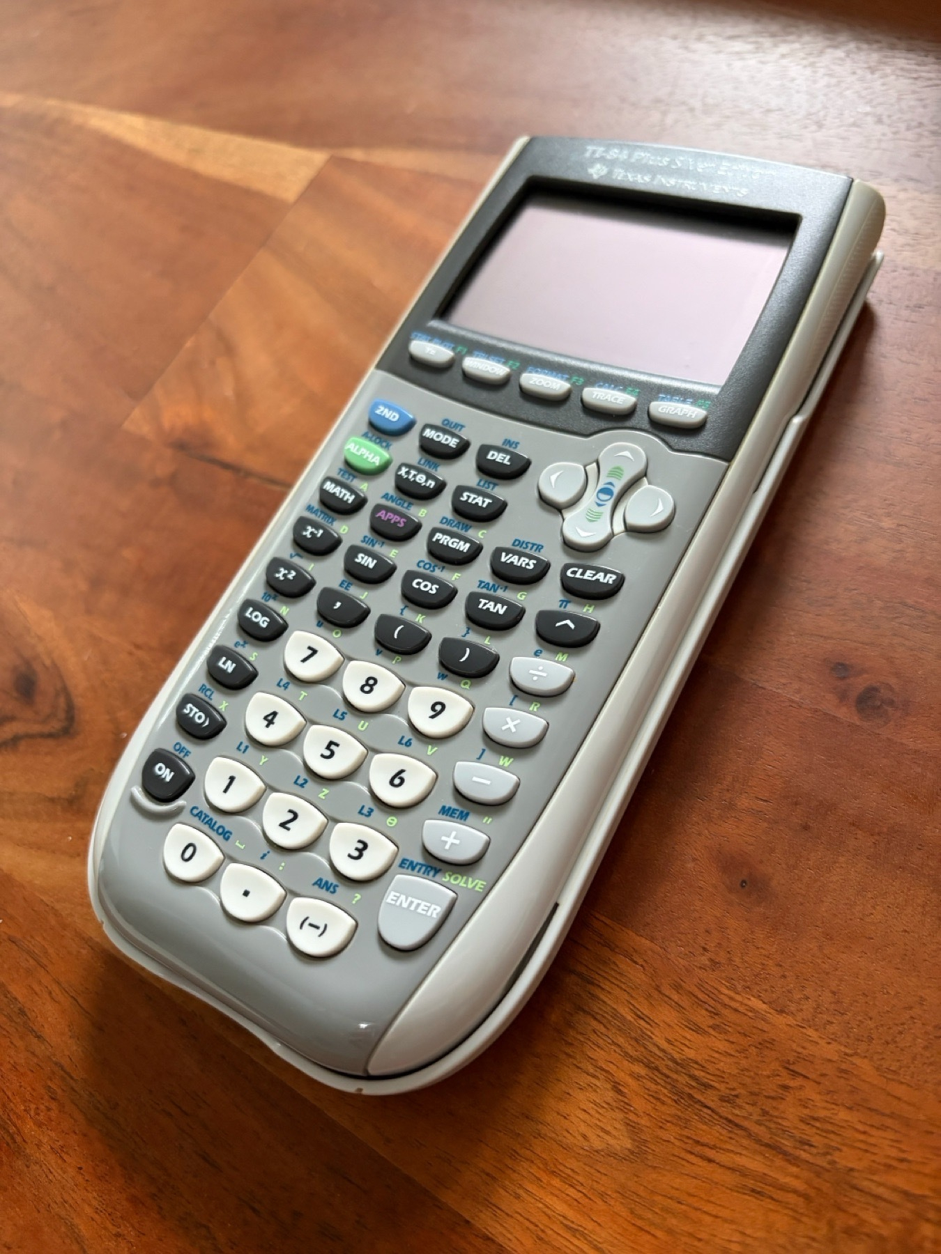A TI-84 Plus graphing calculator, laying on a wooden table.