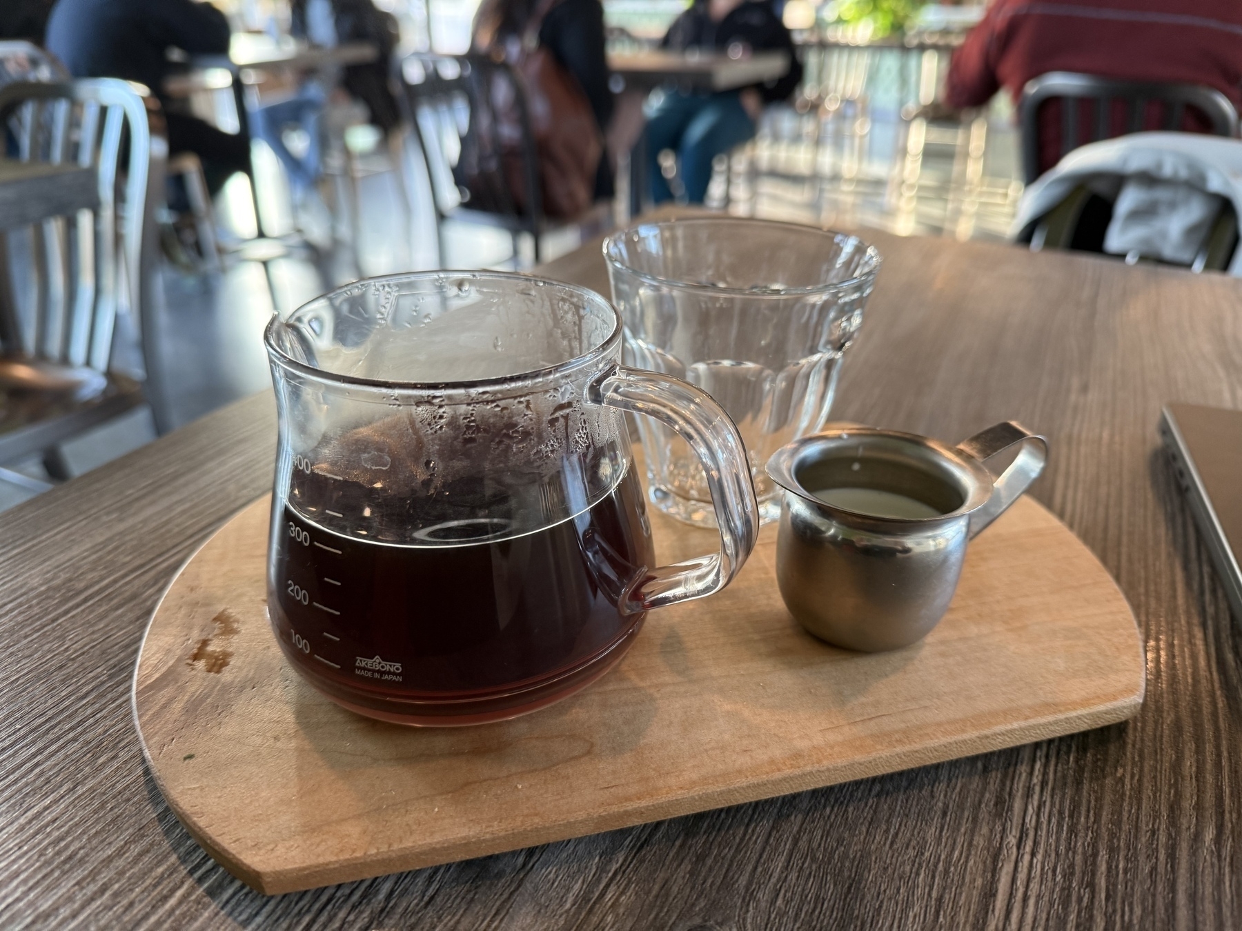 A wooden tray with a graduated glass pitcher of coffee, an empty cup, and a wee pitcher of cream