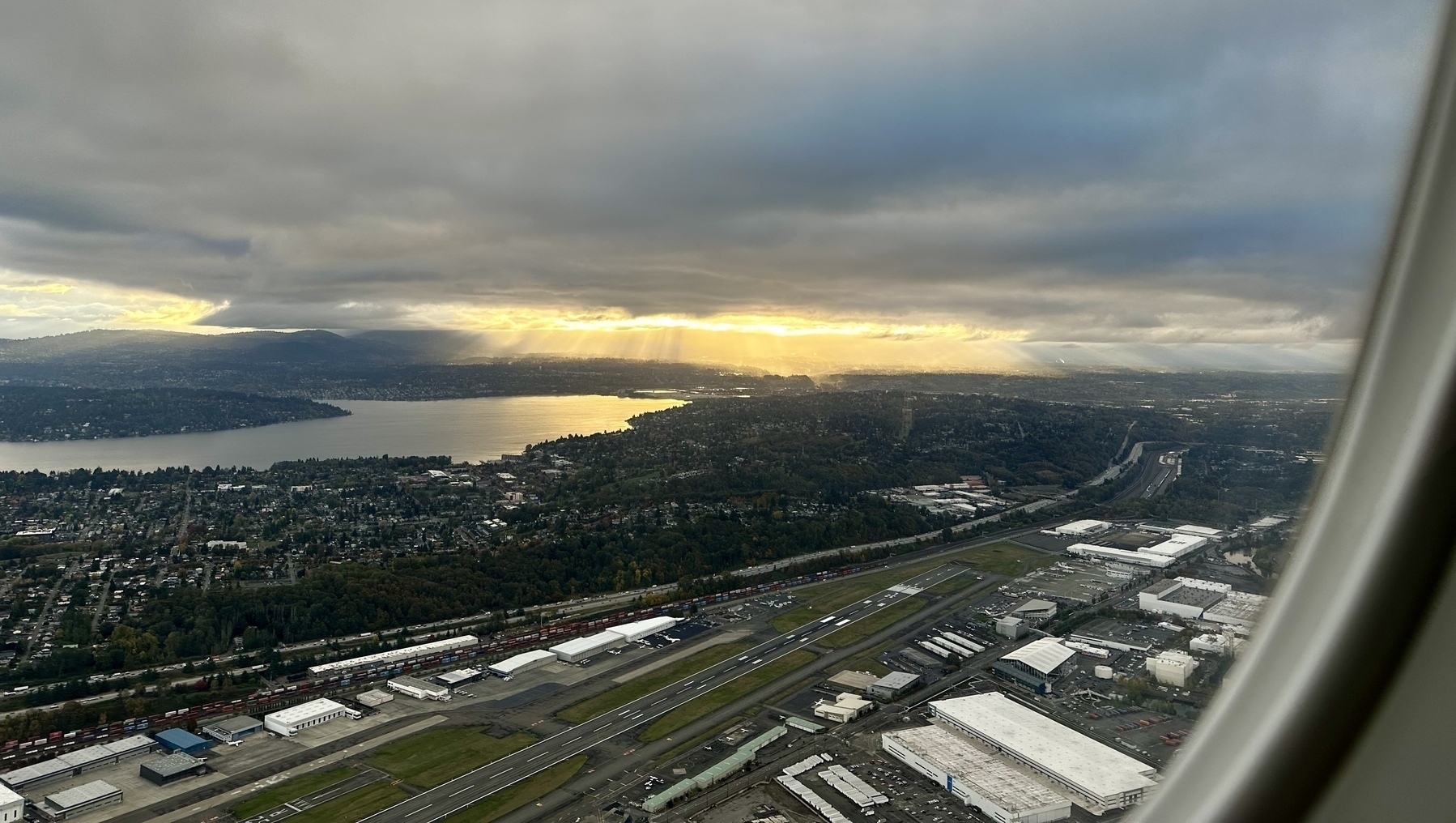 Early morning sun lighting Lake Washington through a gap in heavy gray clouds, framed by airplane window