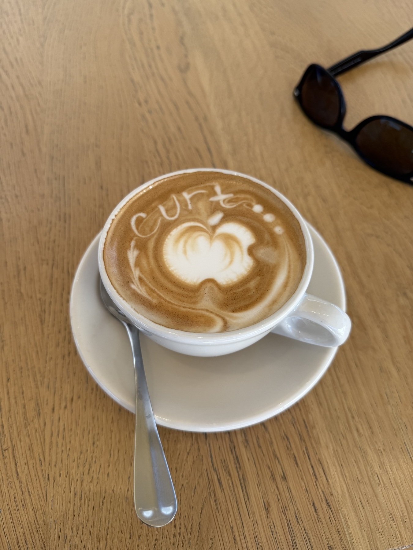 White porcelain coffee cup and saucer. Cappuccino with foam art of my name and the Apple logo. 