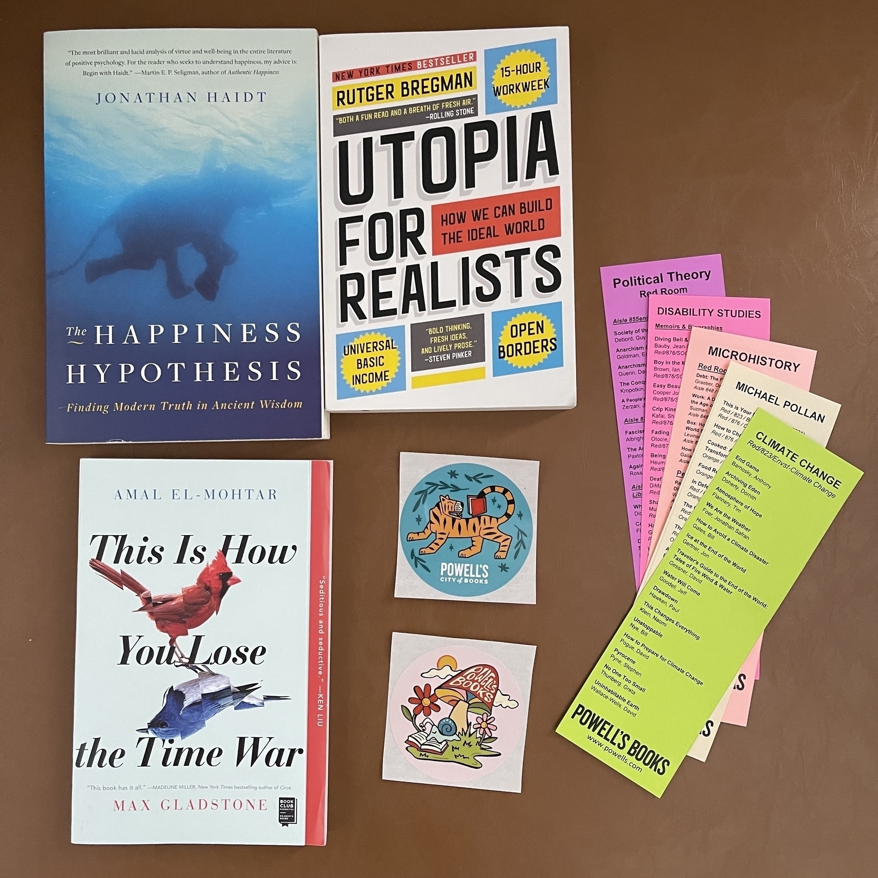 A collection of books, bookmarks, and stickers, featuring titles like The Happiness Hypothesis, Utopia for Realists, and This Is How You Lose the Time War.