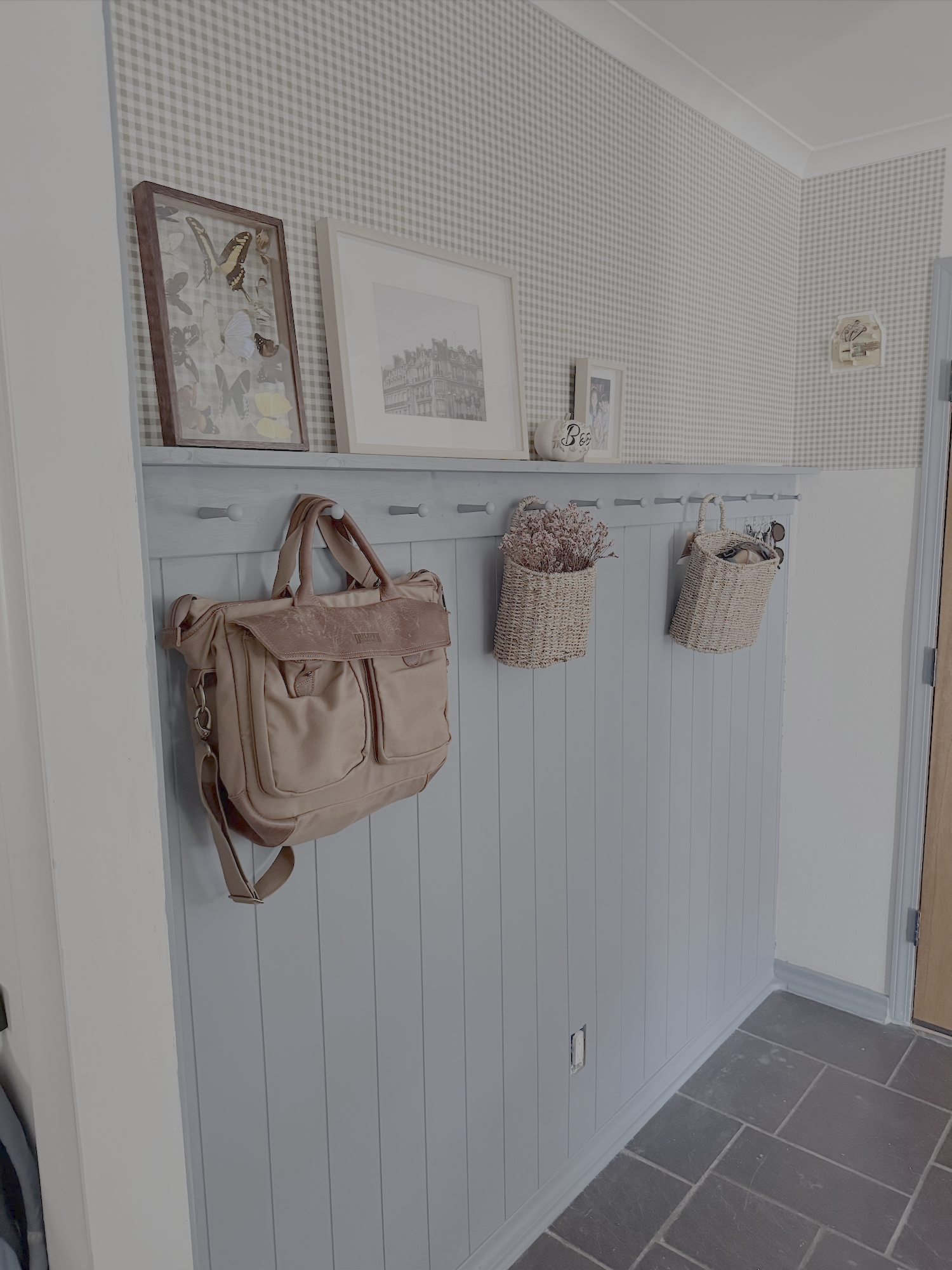 A light blue entryway wall features a hanging leather bag, woven baskets, and framed decorations on top.