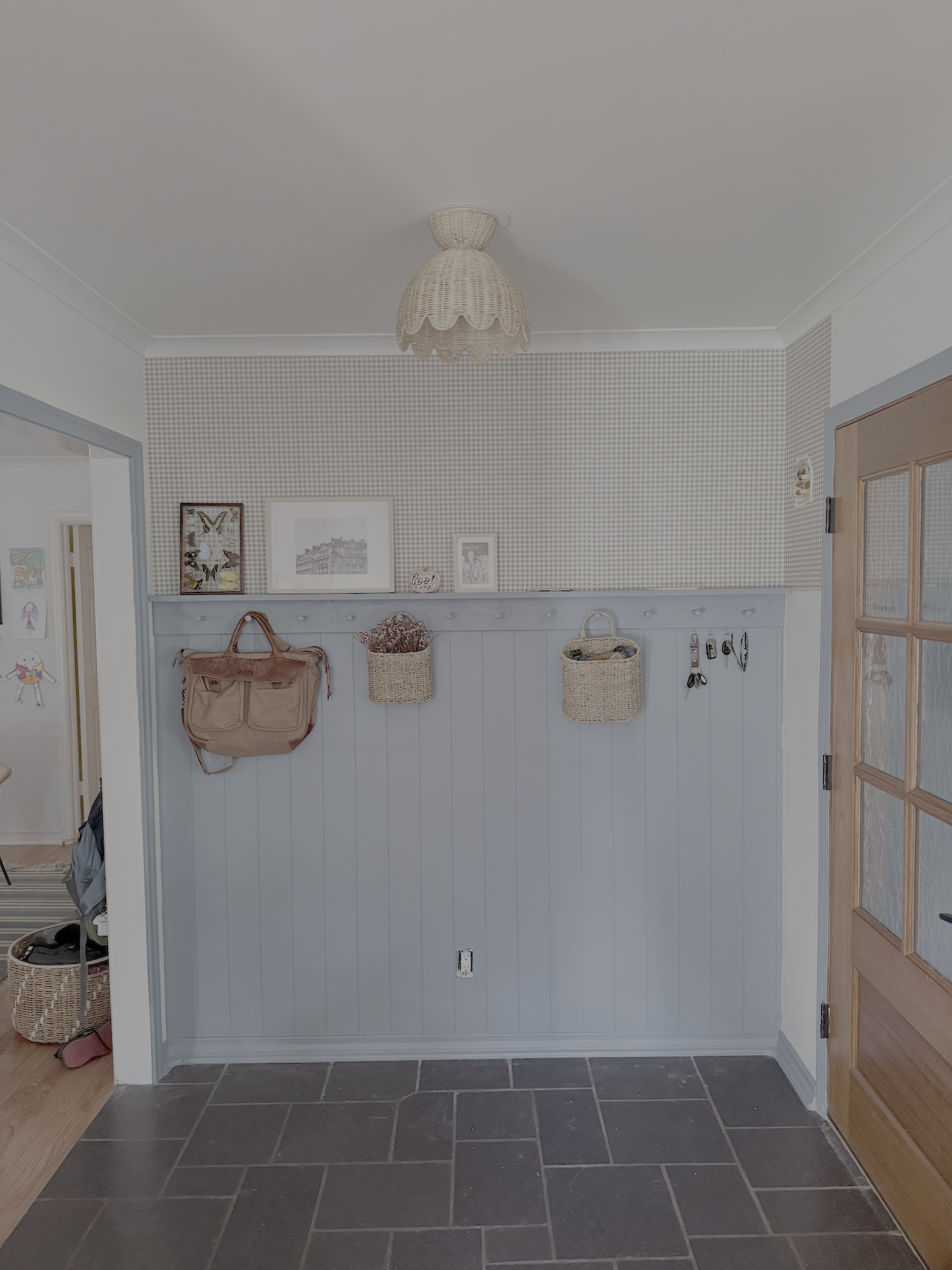 A bright entryway features a wall with hanging baskets, a light fixture on the ceiling, and a wooden door.