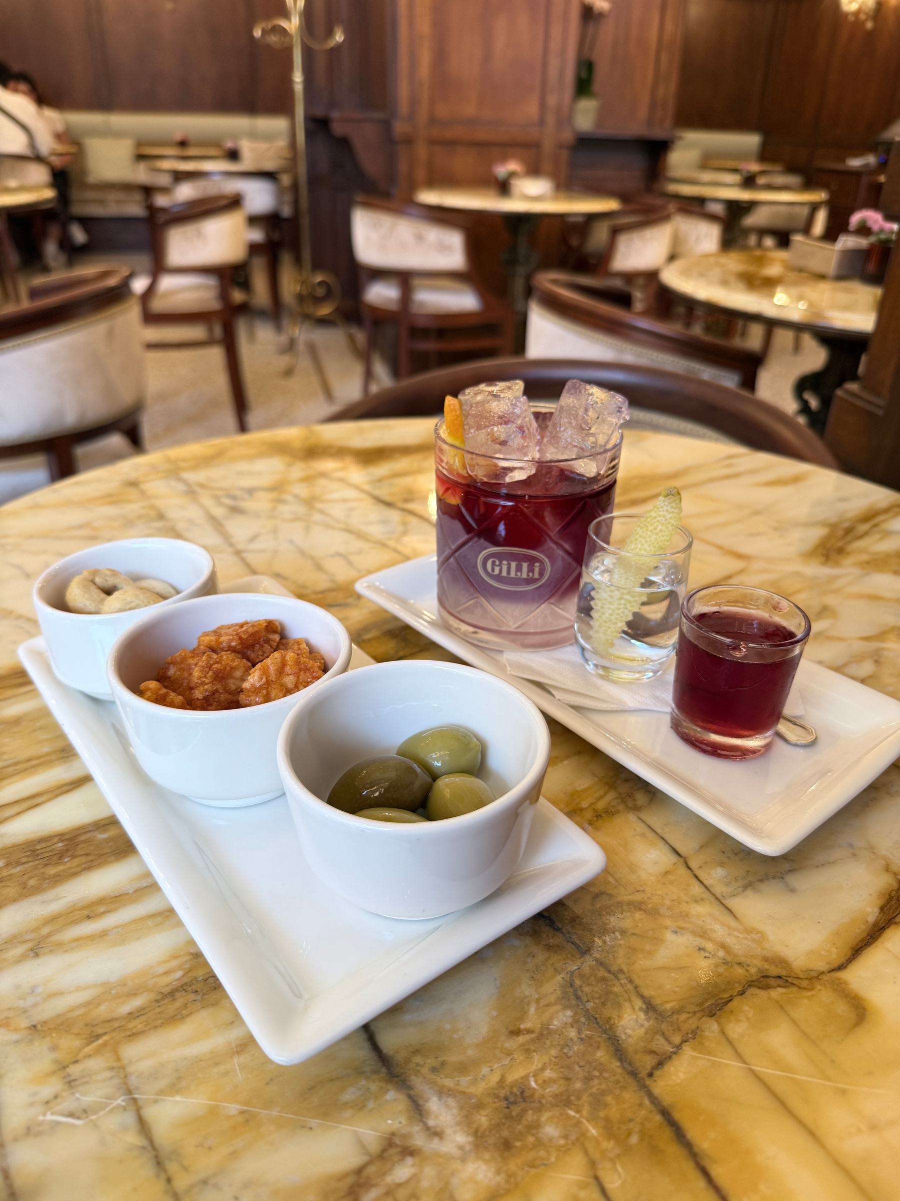 A table with snacks including olives and nuts, accompanied by drinks in a cozy, elegantly furnished setting.
