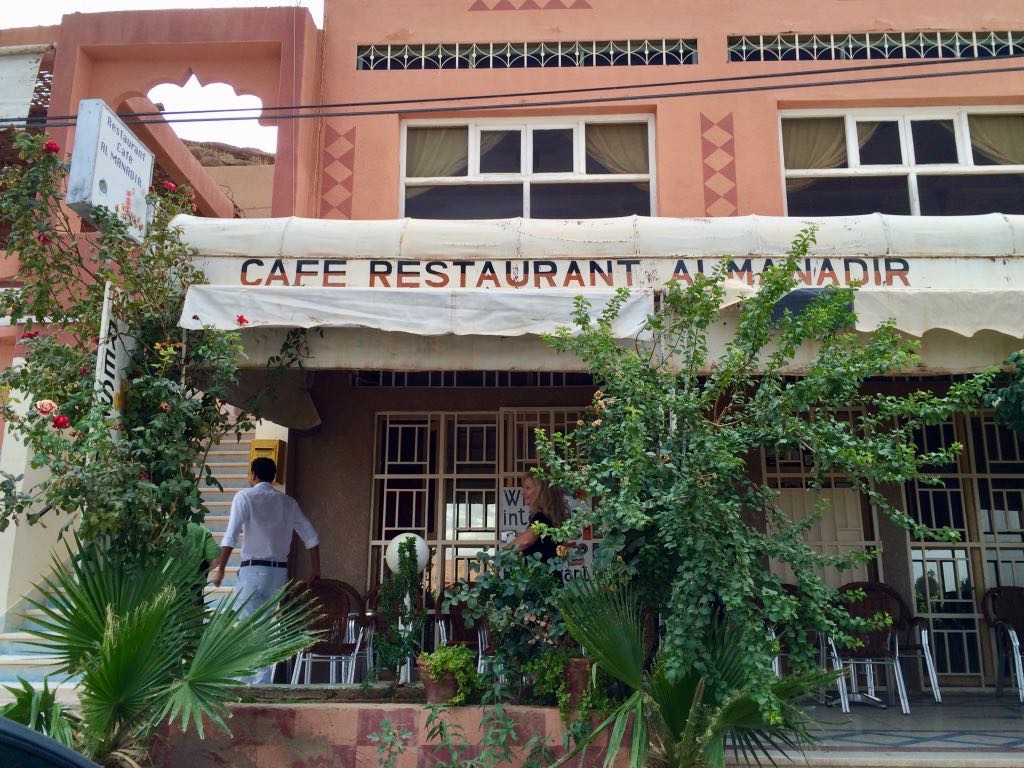 A cafe restaurant named Al Manadir is shown with a partially covered outdoor seating area surrounded by greenery.