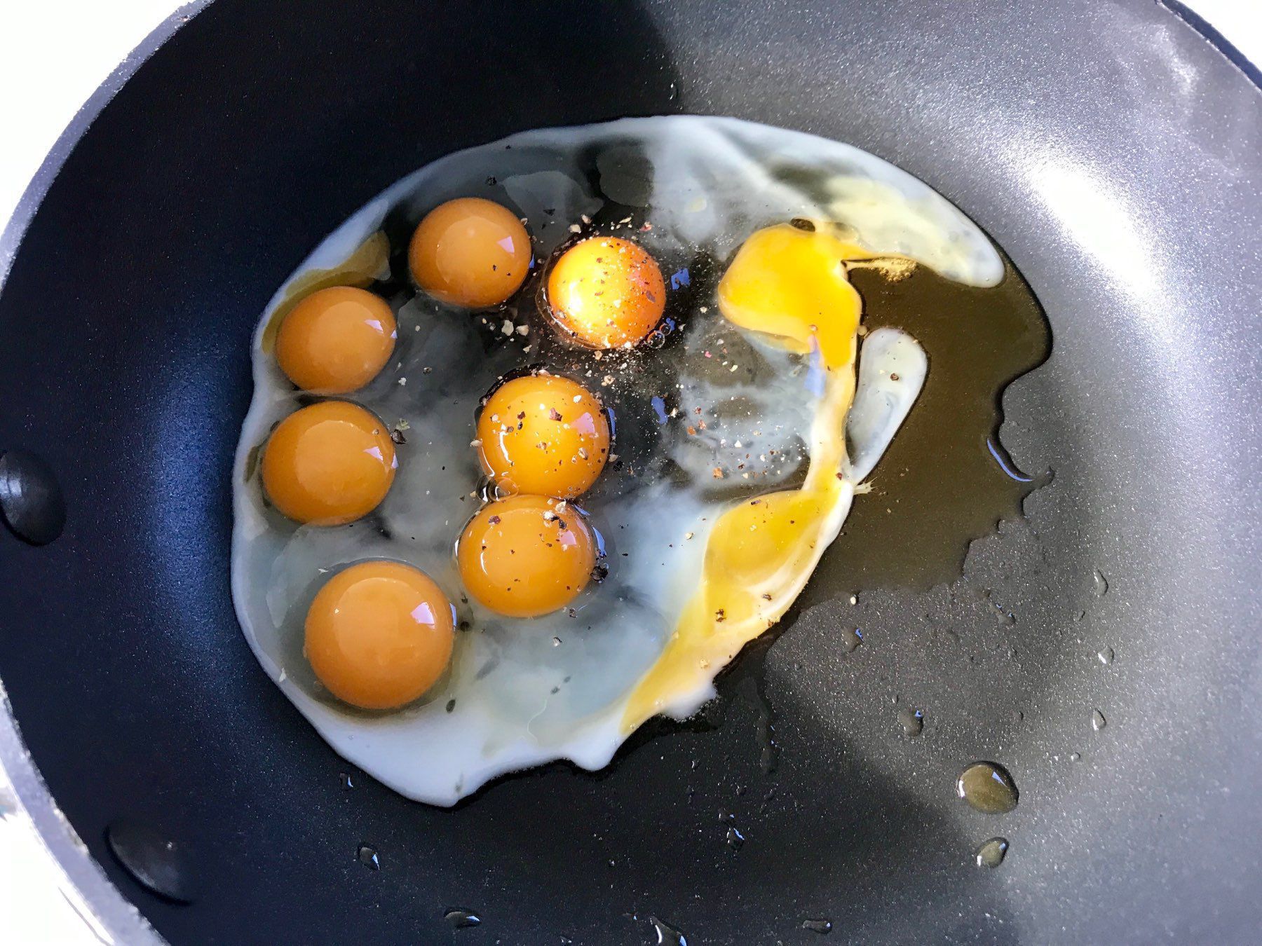 Several egg yolks are being cooked in a frying pan, with one yolk broken and spreading with the egg white.