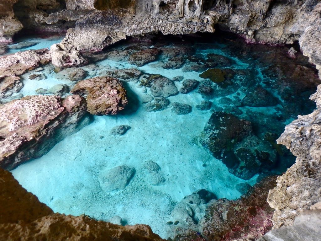 A natural pool of clear turquoise water is surrounded by rugged rock formations inside a cave.