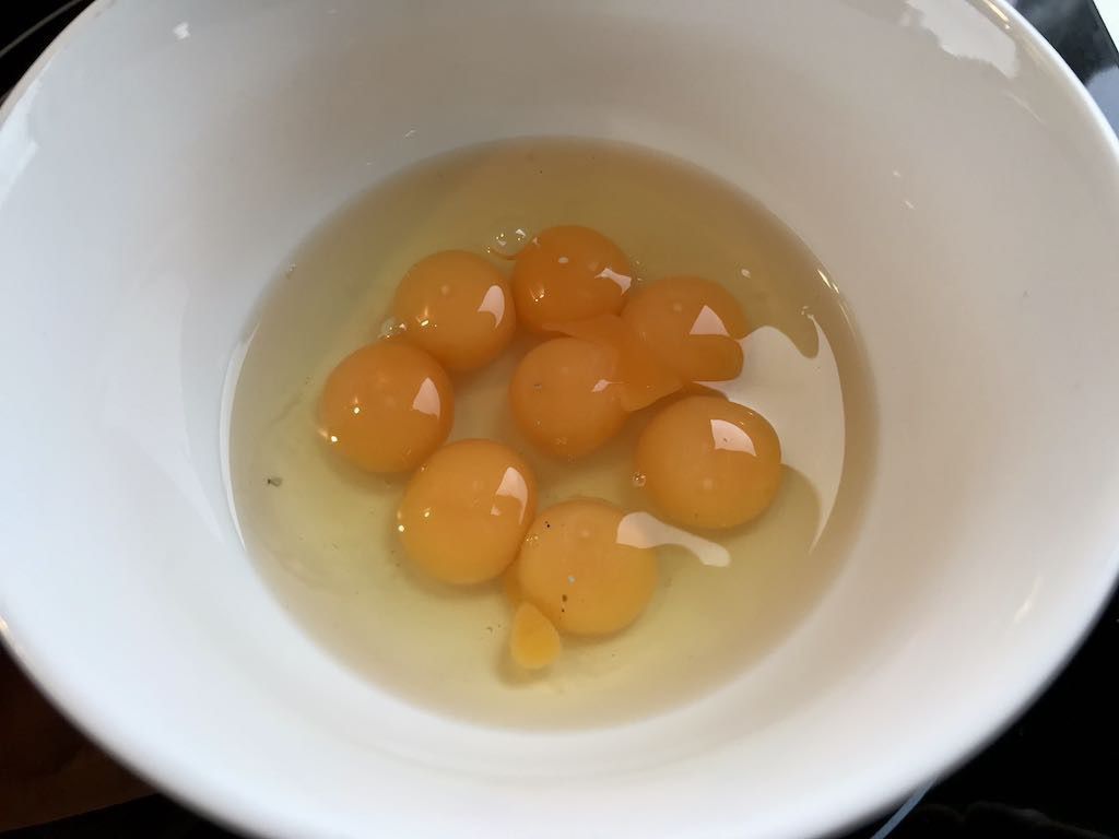 A white bowl contains multiple raw egg yolks and egg whites.