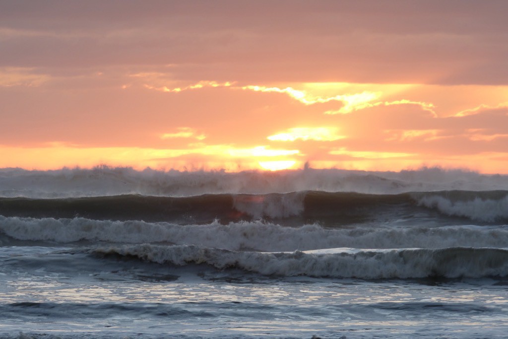 Big waves in the foreground, with orange sky.