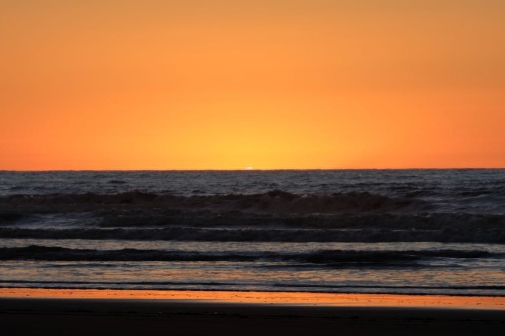 Across the sea. The sun is below the horizon with a hint of a ‘flag’ remaining. 