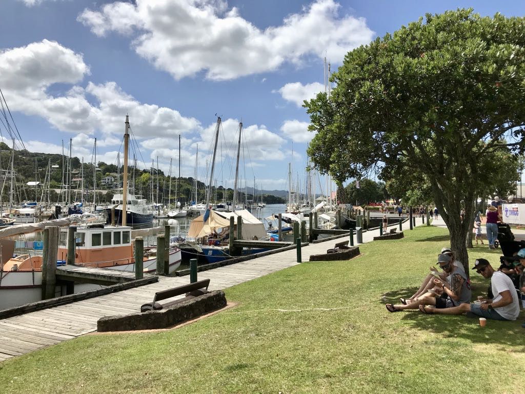 People sitting on grass beside a marina. 