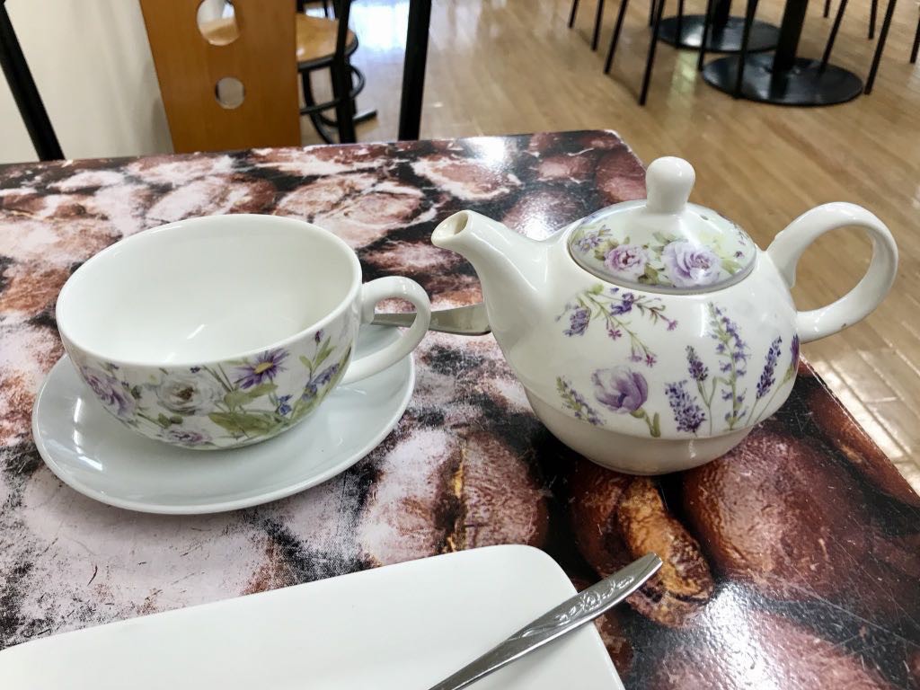 White teapot with painted flowers next to the teacup.