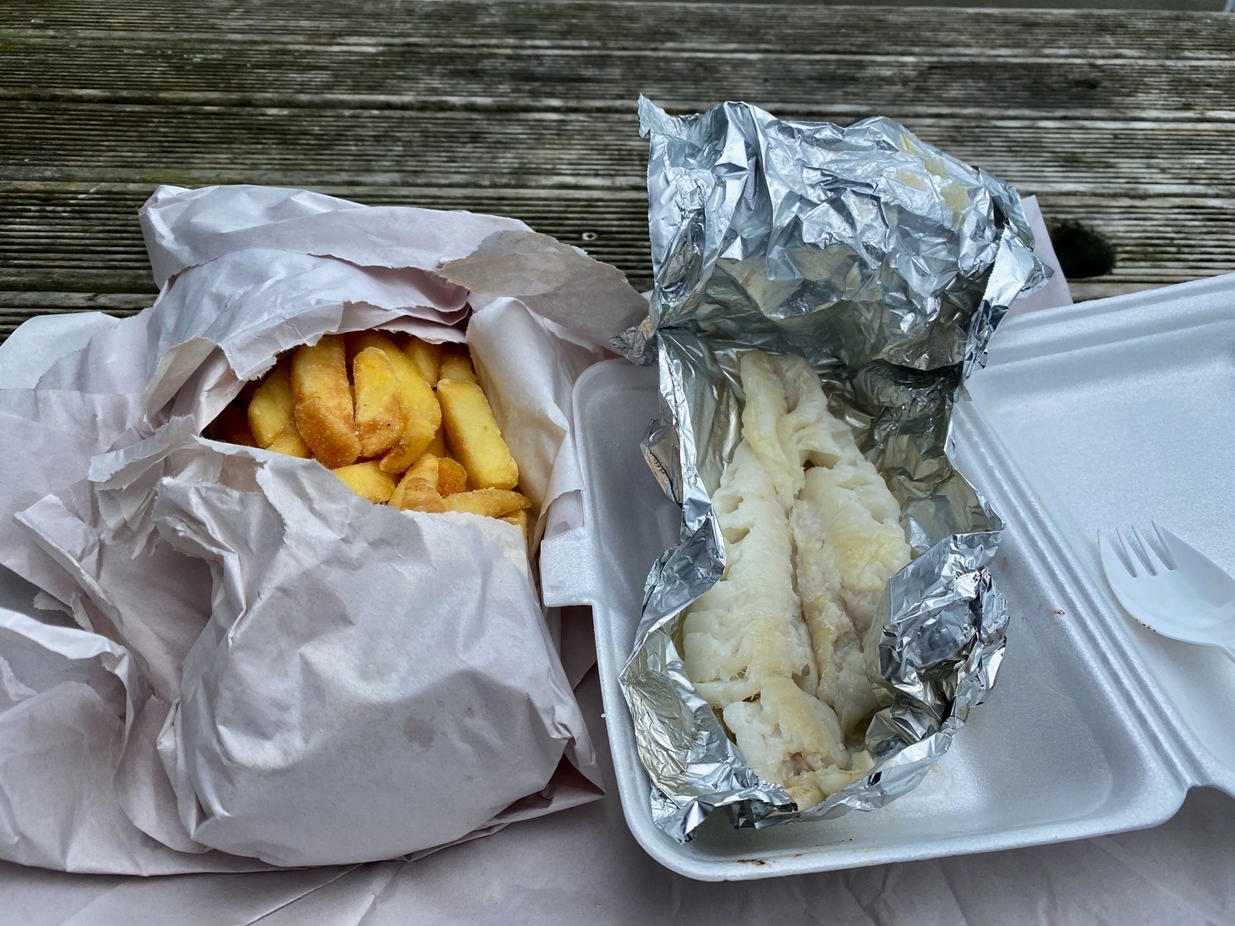 Chips wrapped in papaer; fish in foil in  a polystyrene pack and with plastic fork.