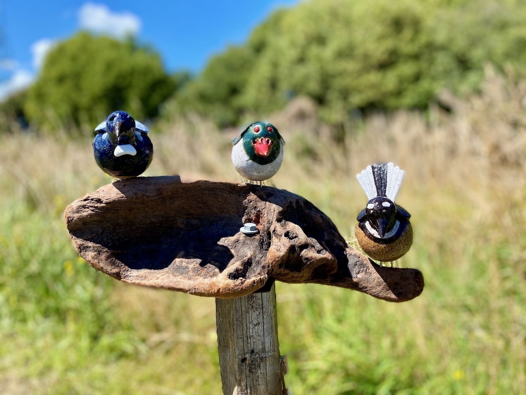 3 ceramic birds perched on driftwood. 