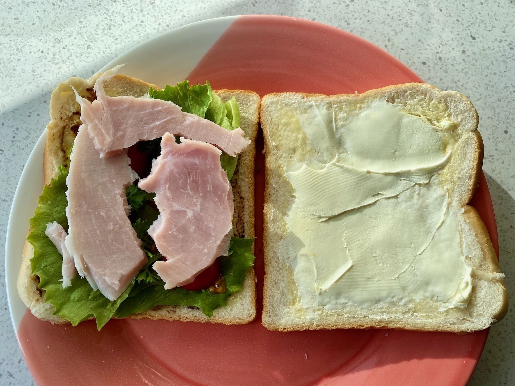 Lettuce, tomatoes and ham on the bread, with another slice that has cream cheese on it. 