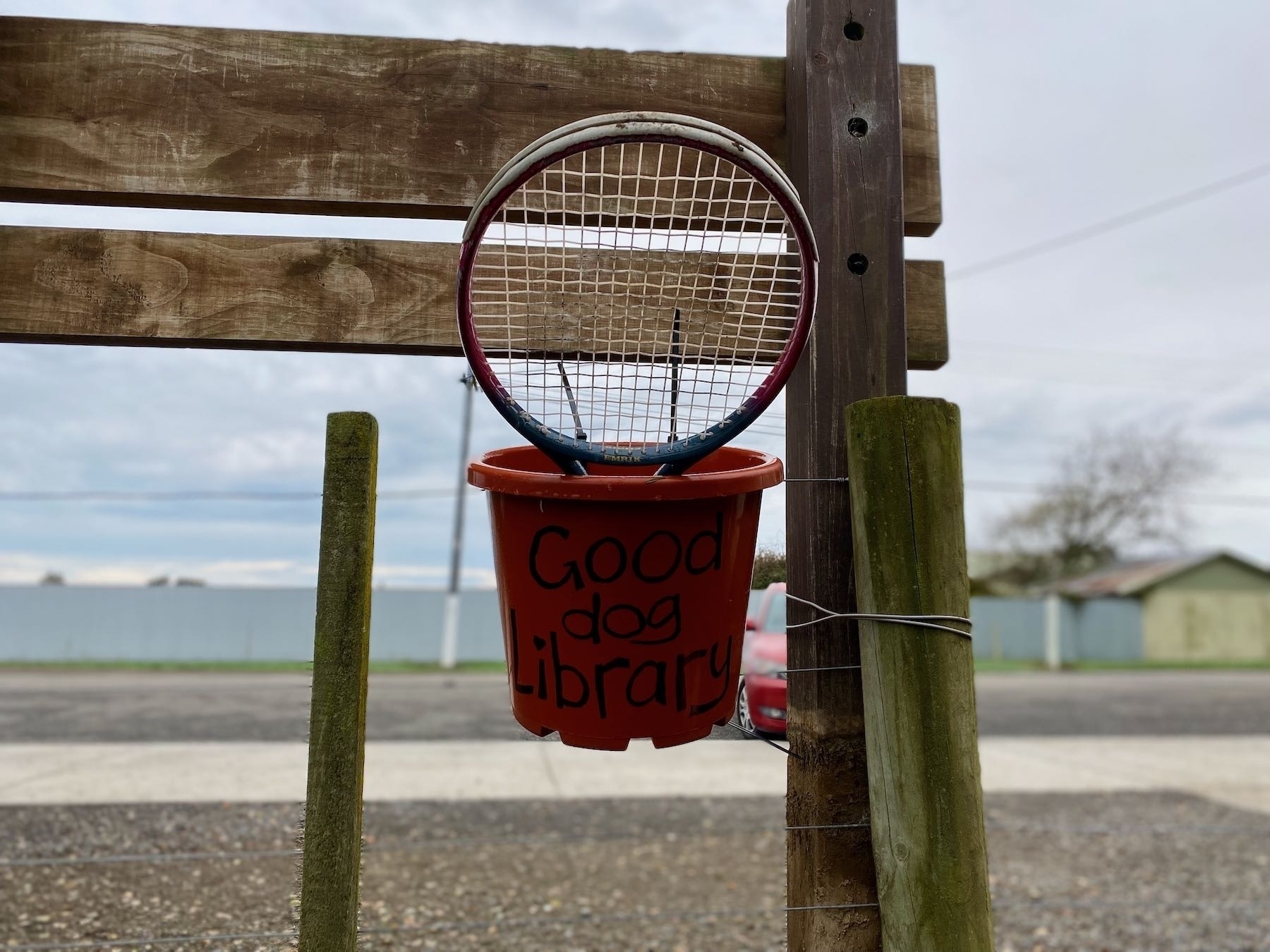 Bucket labelled Good Dog Library, with a tennis racket in it. 
