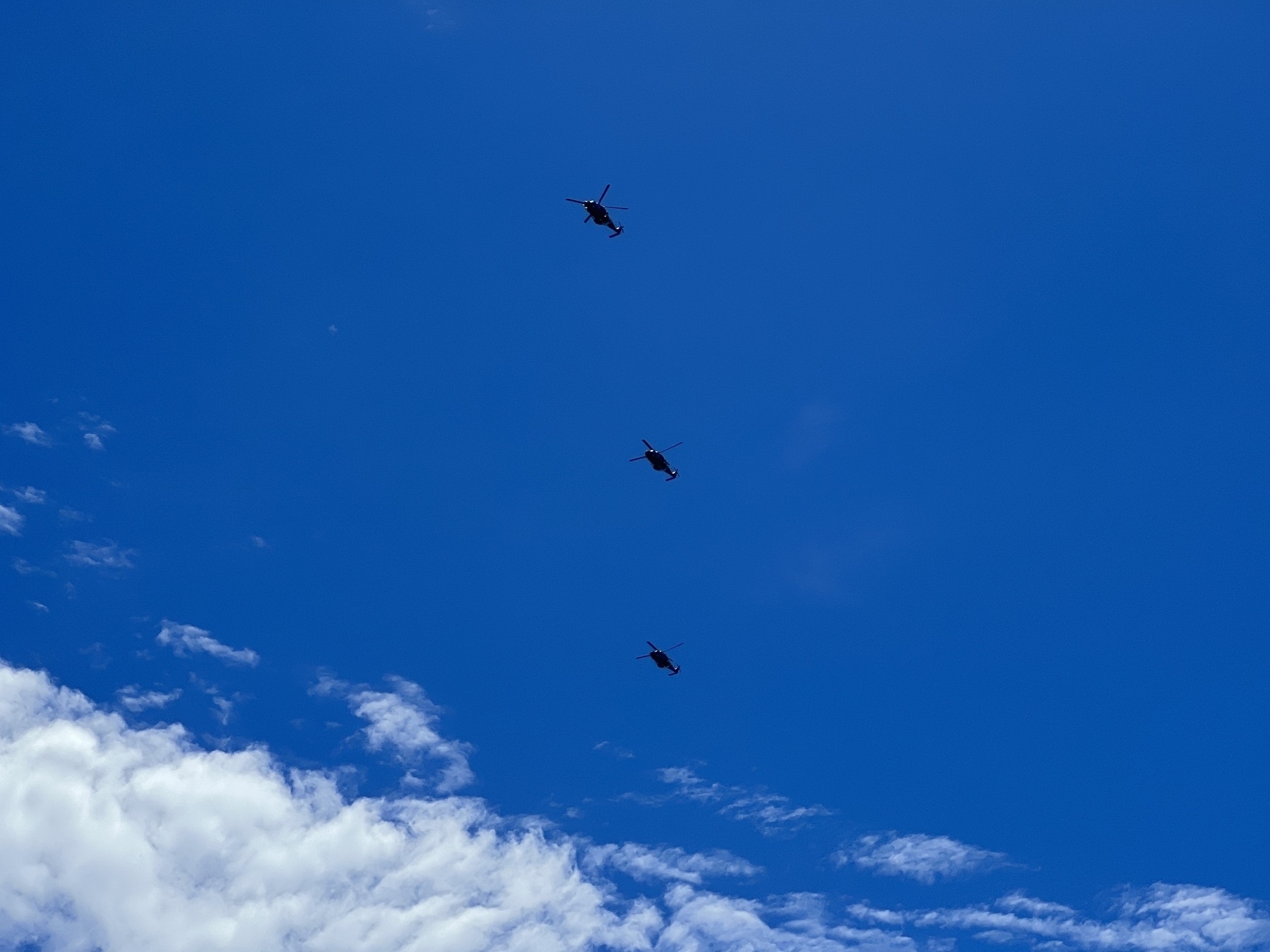 Three military helicopters in formation overhead. 