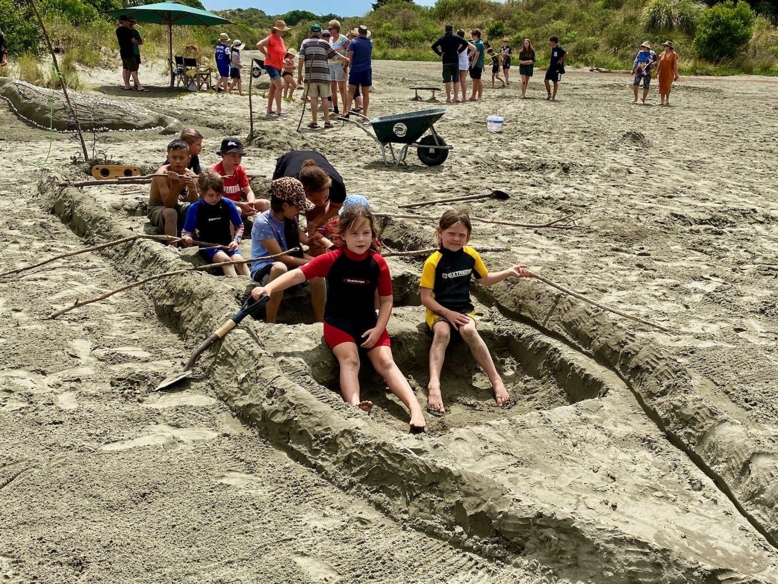 Children sit in a canoe made of sand. 