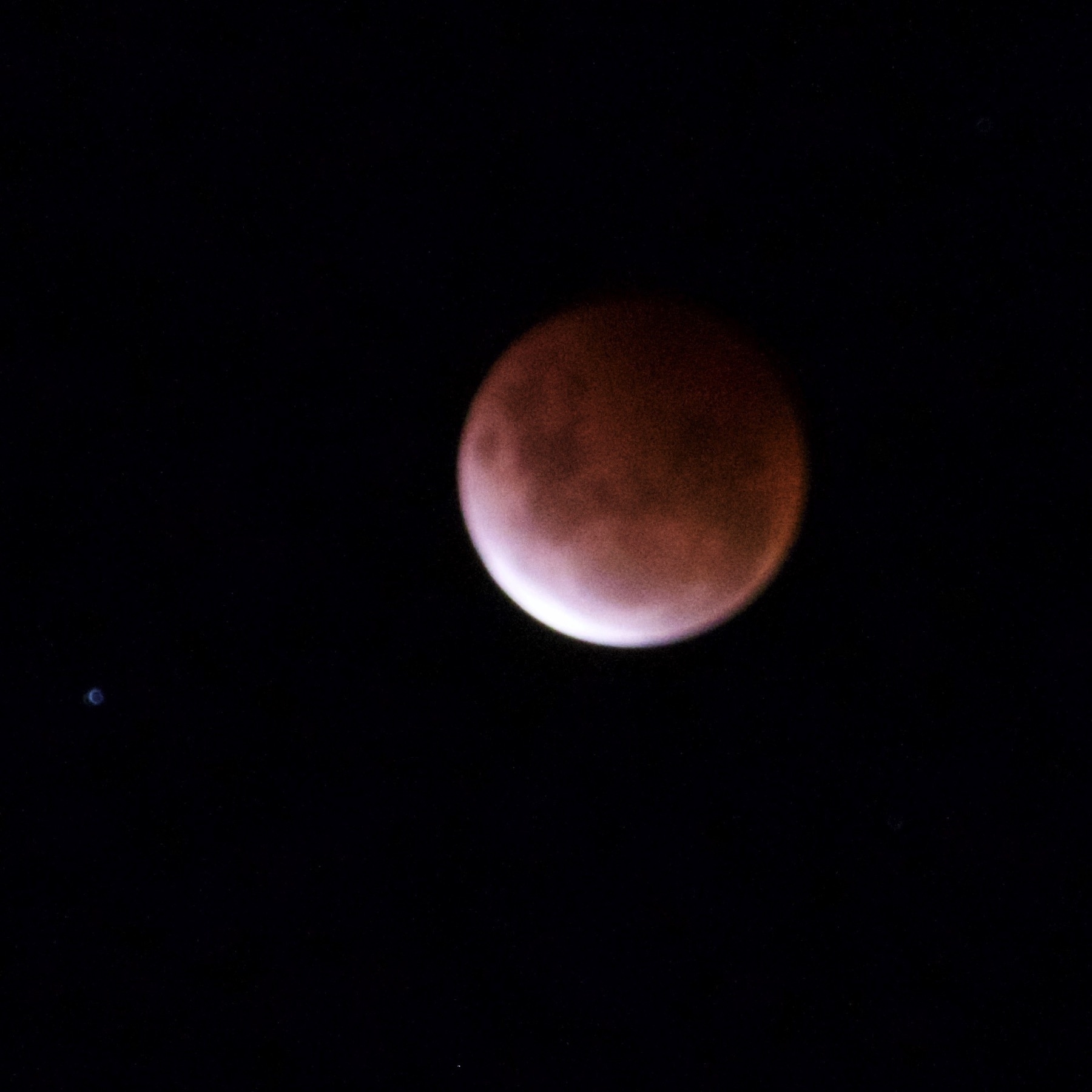 Red-tinged moon with a sliver of white at bottom left. 