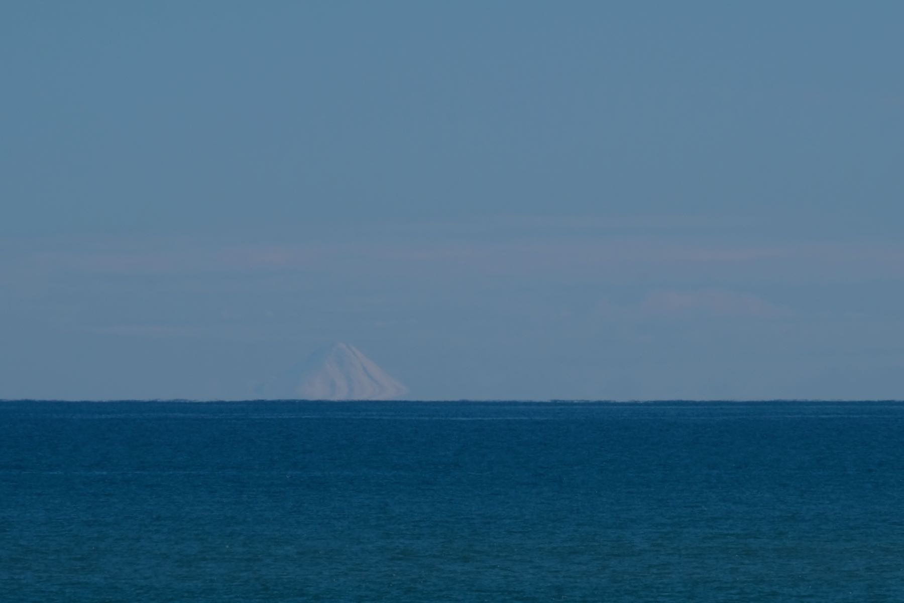 White snow clad conical mountain across the sea. 
