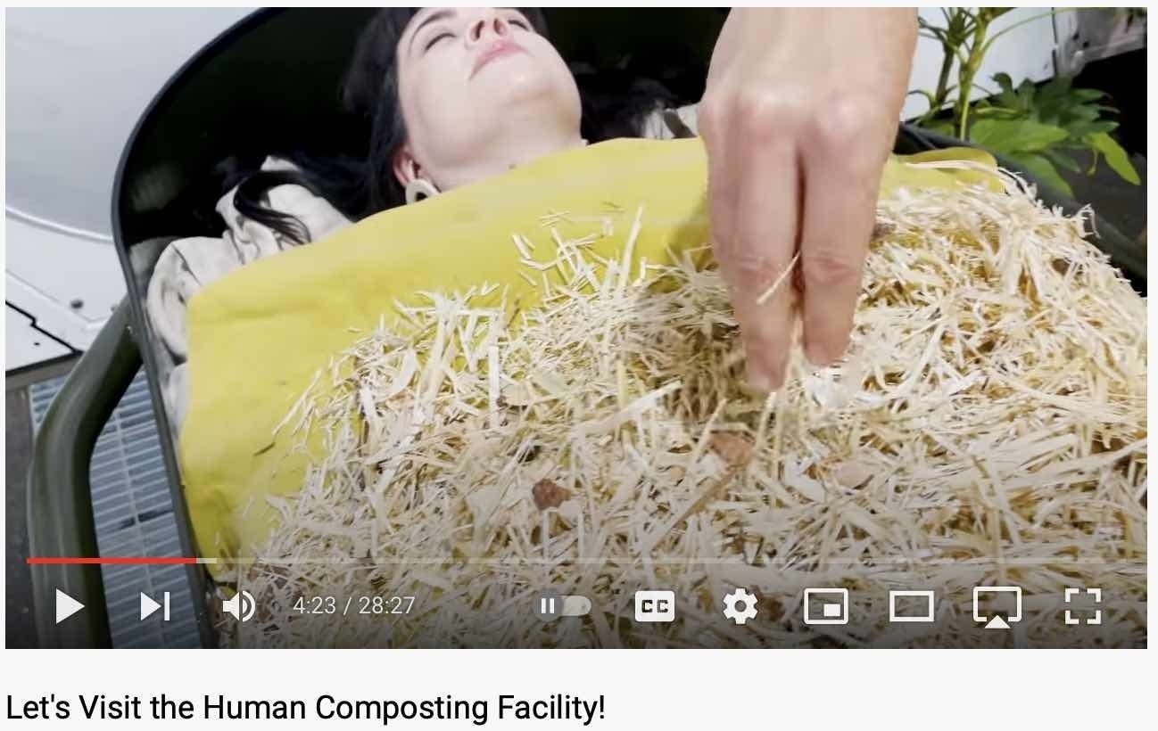 An actor in a coffin being covered with composting material. 