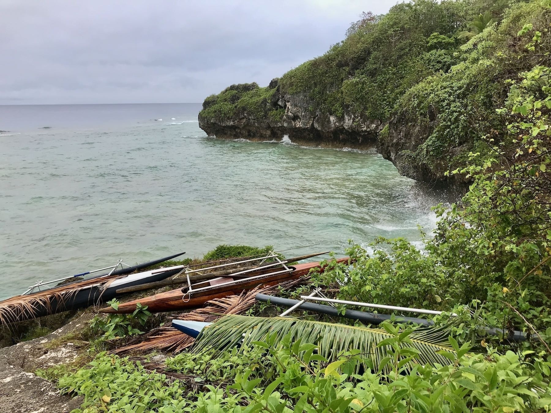 Outrigger canoes high above the water by steep rocky cliffs. 