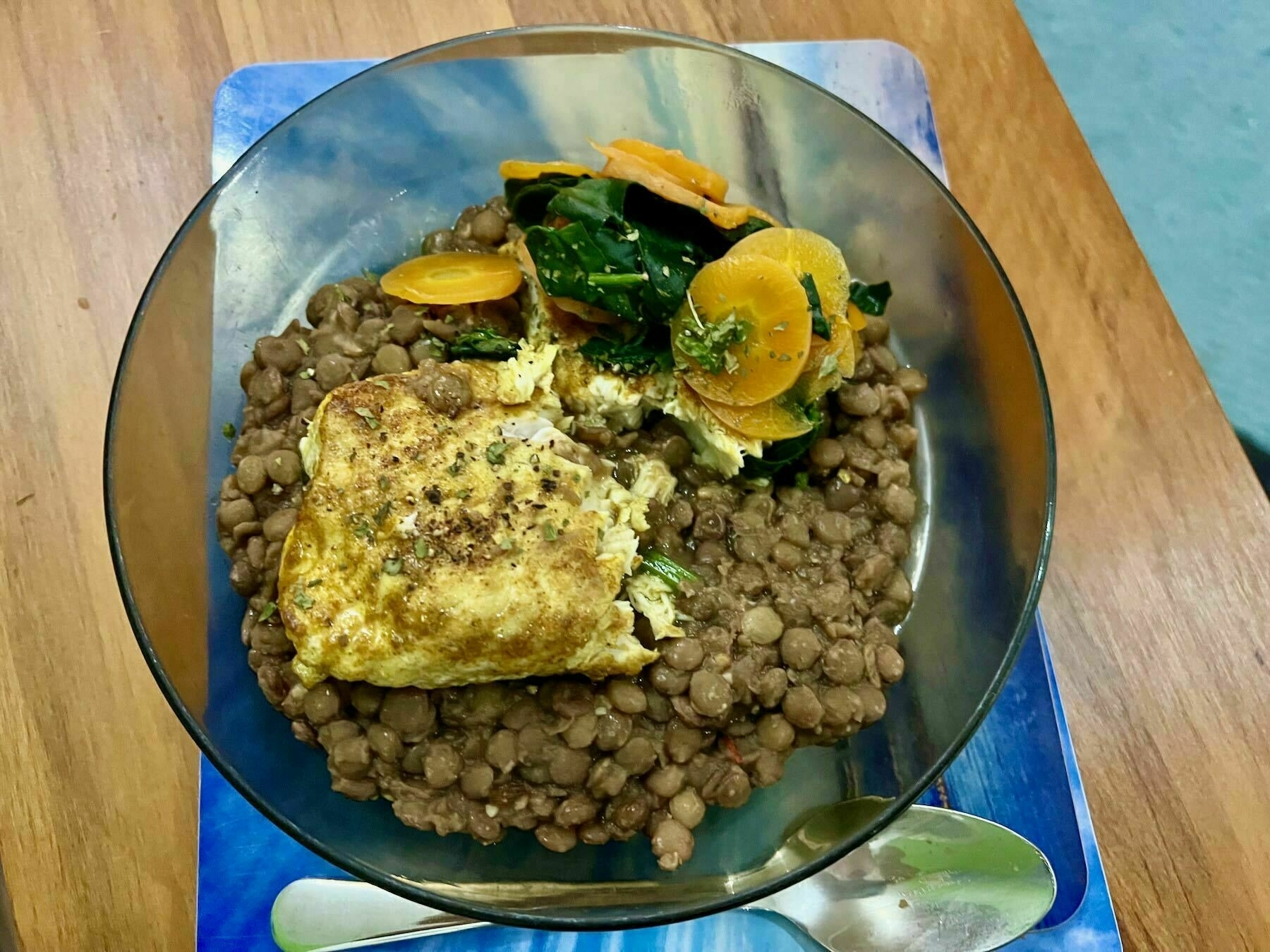 Cooked fish on a bed of lentils, with spinach and carrot. 