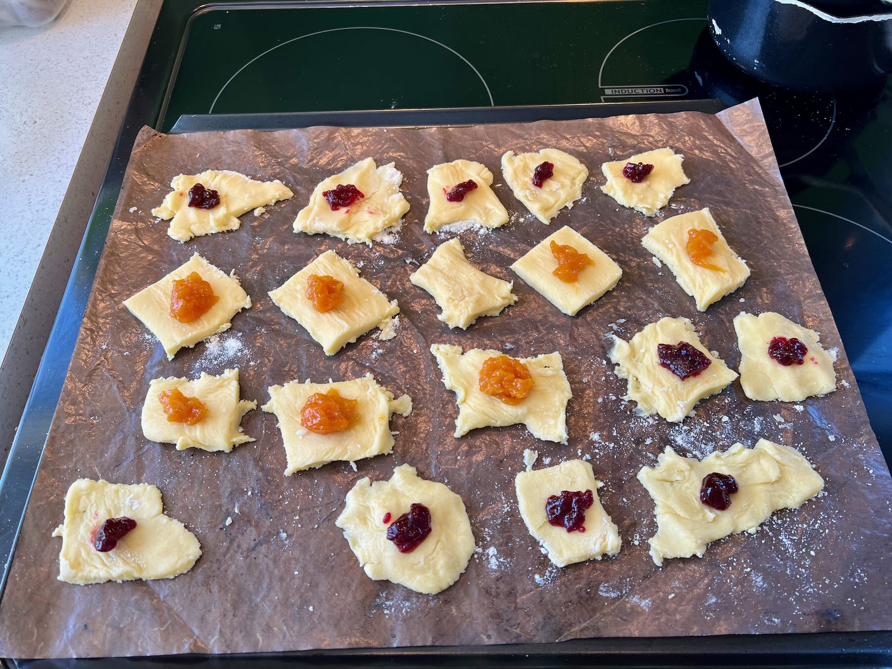Squares of raw pastry on a tray with a dob of jam on each square. 