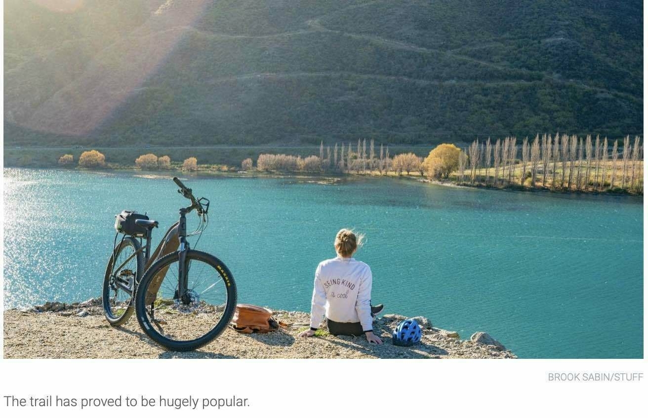 Bike parked and woman sitting beside an astonishingly blue lake in beautiful surroundings. 