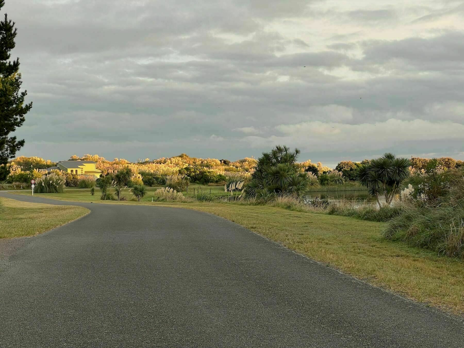 Road leading to sunlit dunes and house, with darker foreground. 