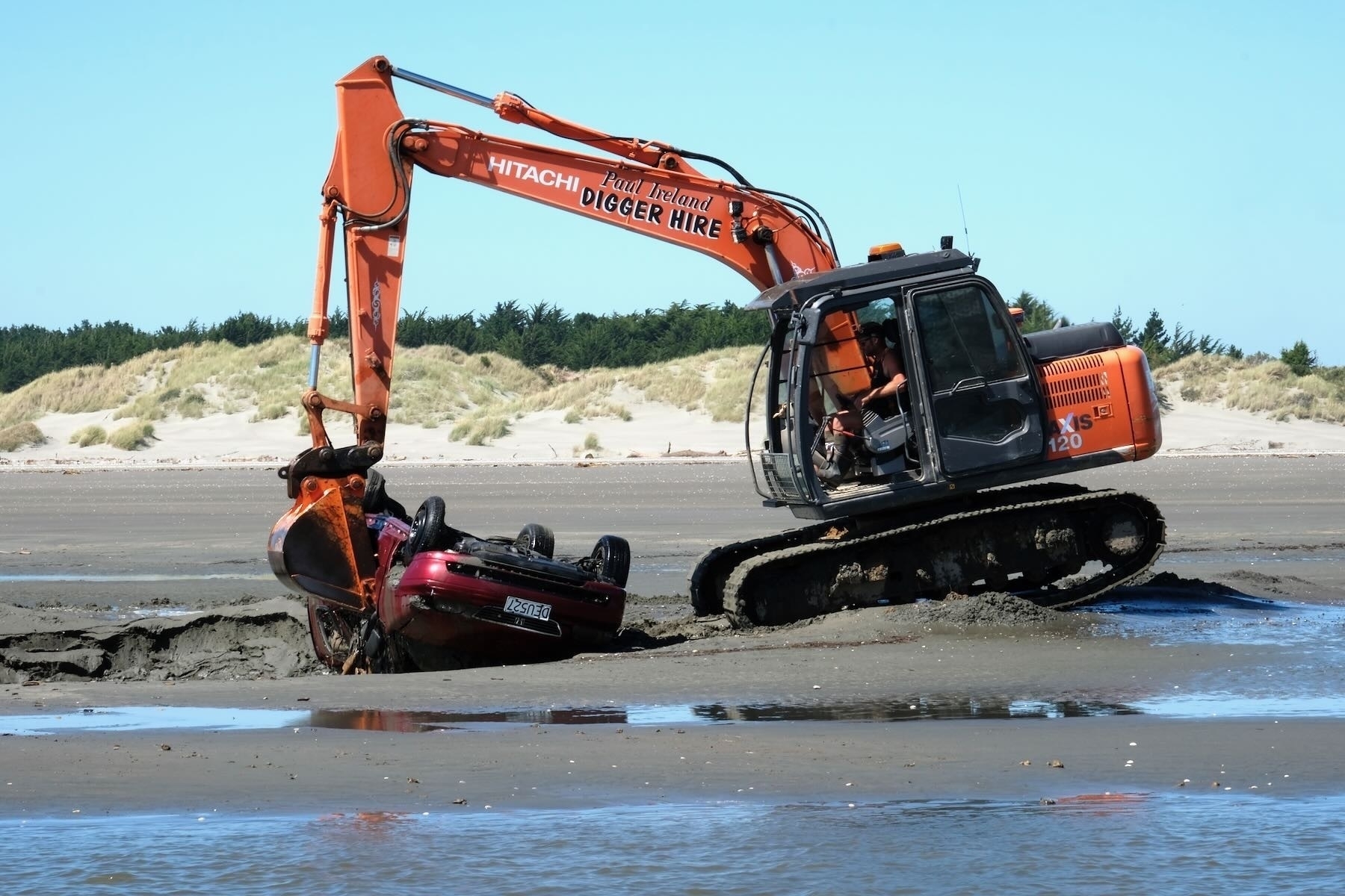 Digger removes abandoned car stuck in the sand. 