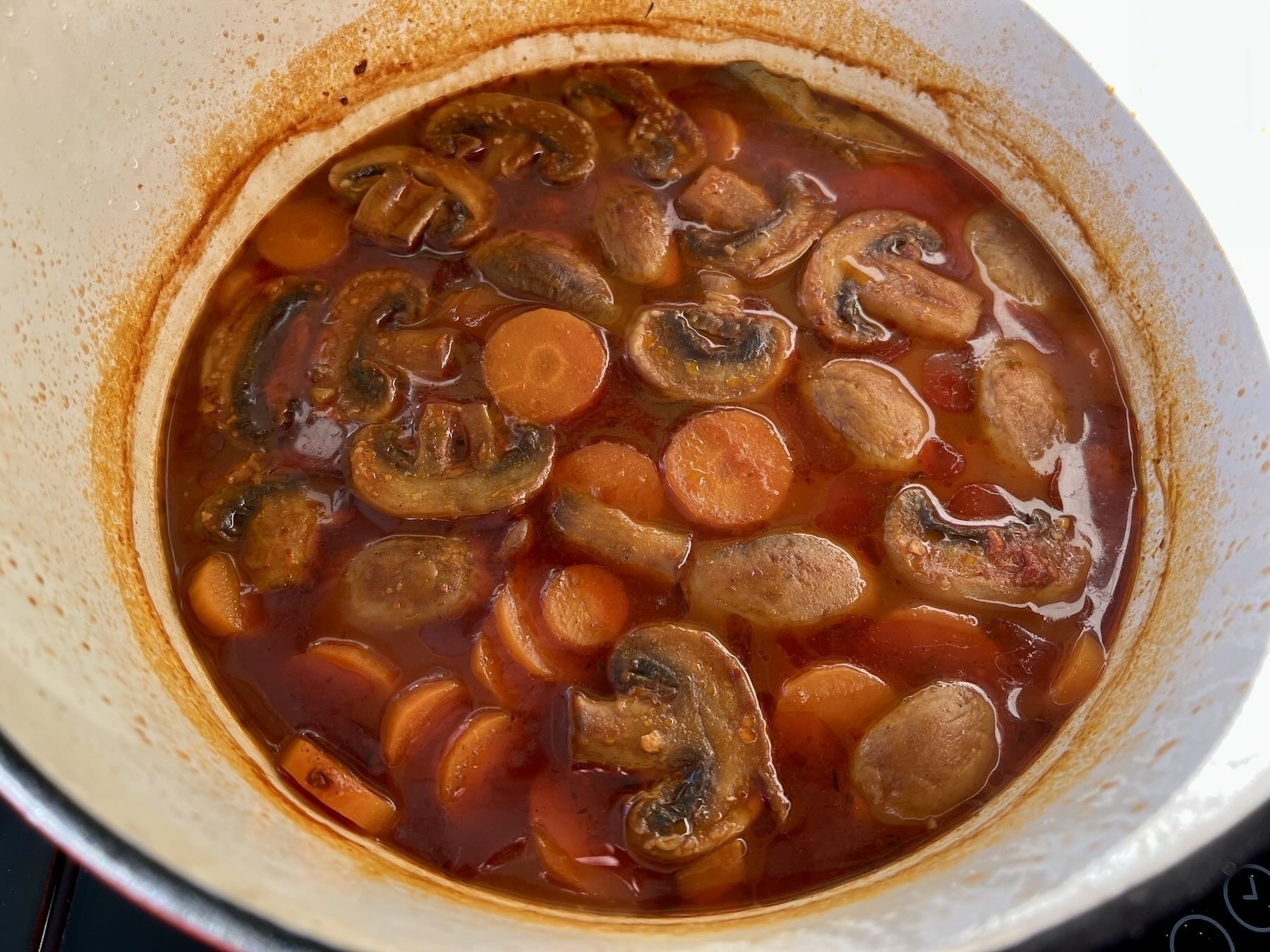A casserole dish with mushrooms, tomatoes, sauce on top of unseen chickpeas. 