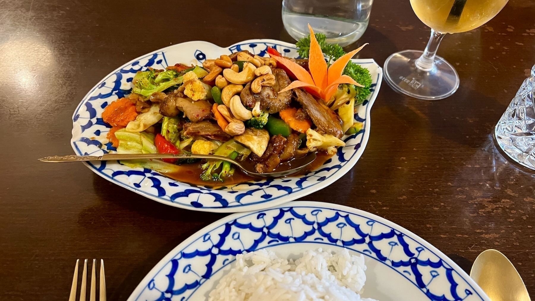 Colourful dish of vegetables, nuts and meat, with a plate of rice beside. 