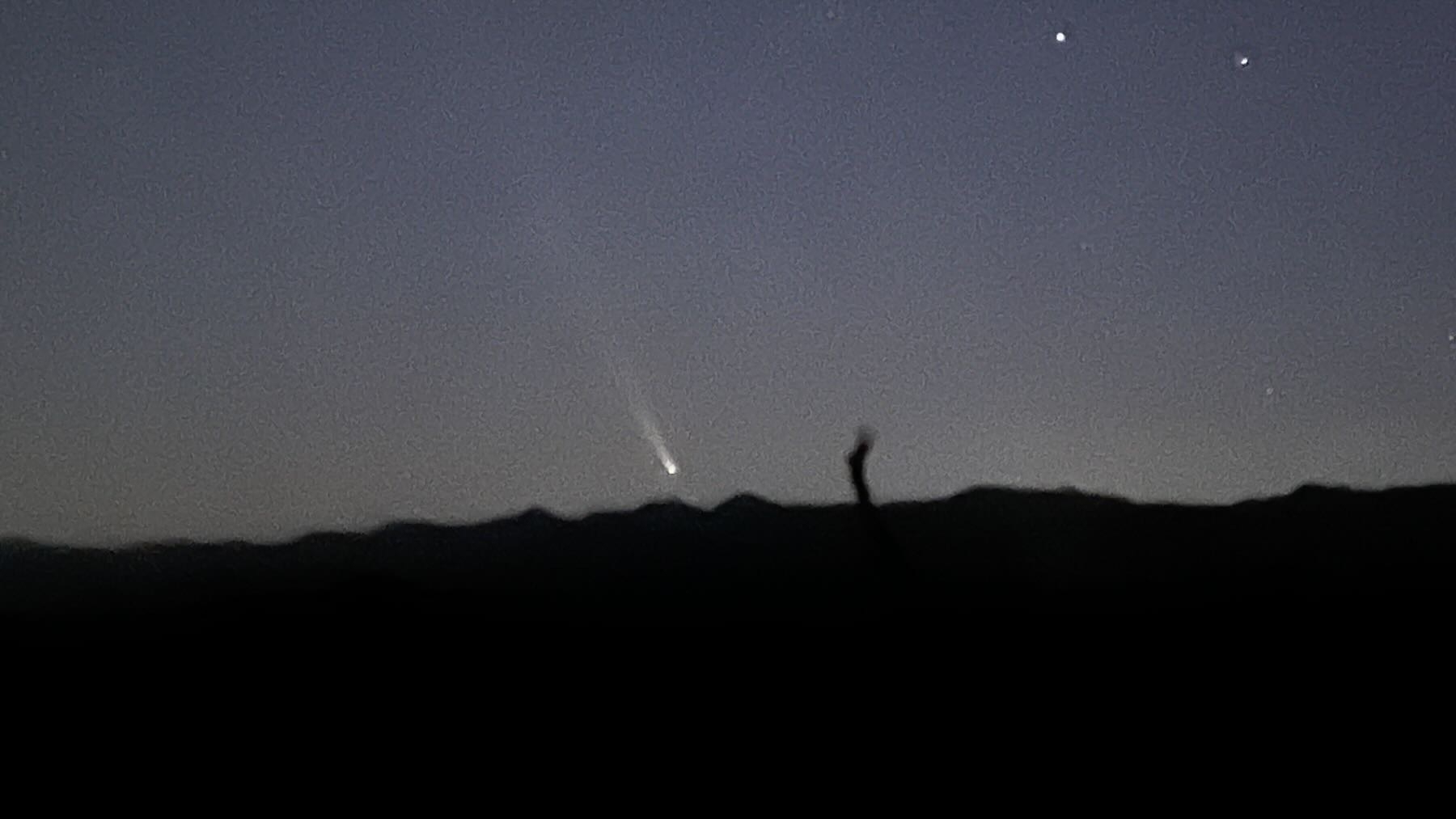 A long bright streak above a dark hilly horizon. 